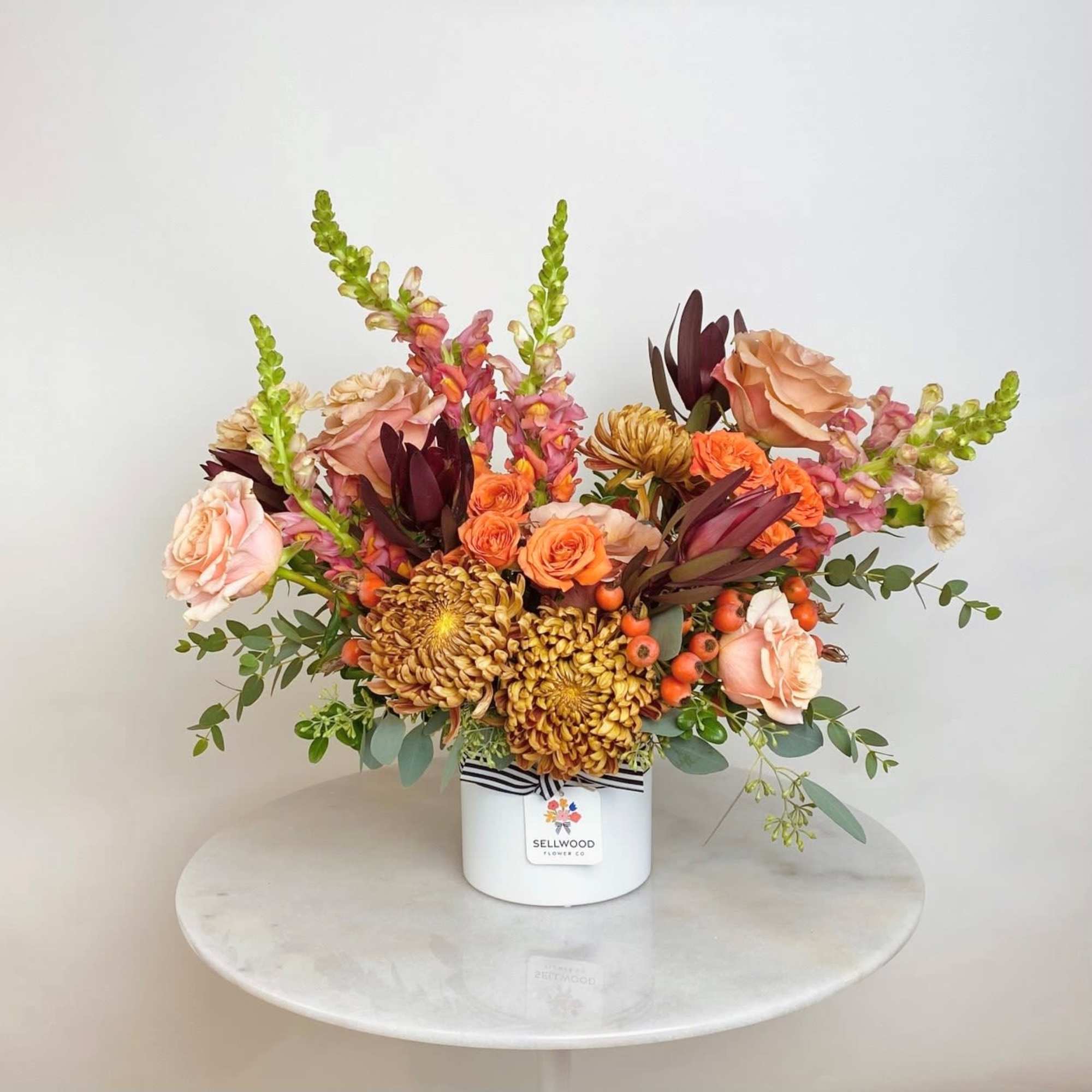 This lush autumn arrangement exudes warmth with a rich blend of mums