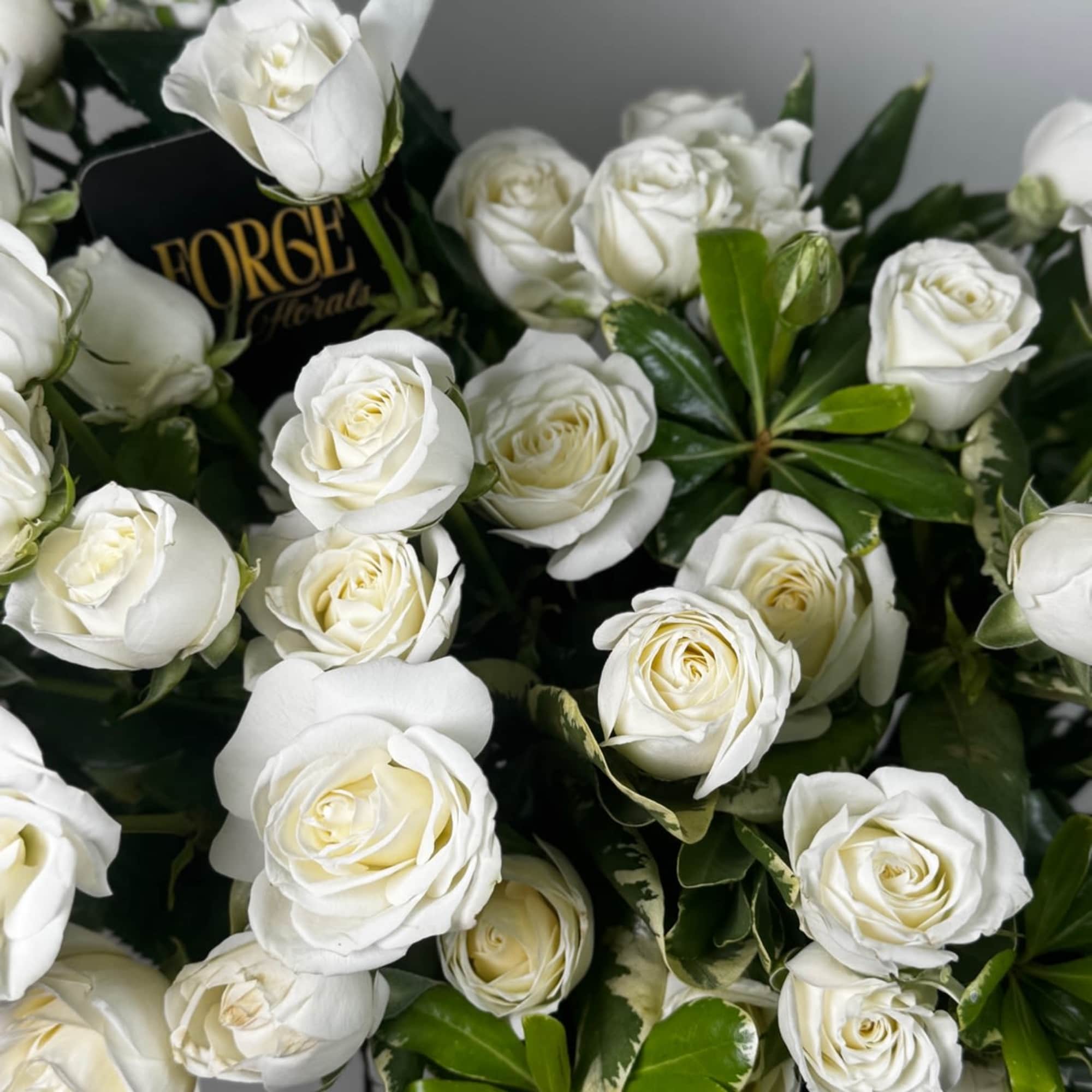 Bold white spray roses arranged with lush greenery in a matte-gold vase.