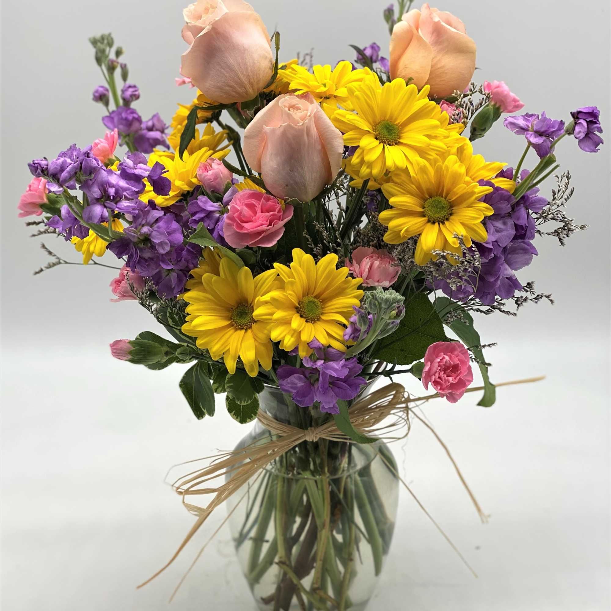 A bright combination of yellow daisies, purple stock, peach roses and pink