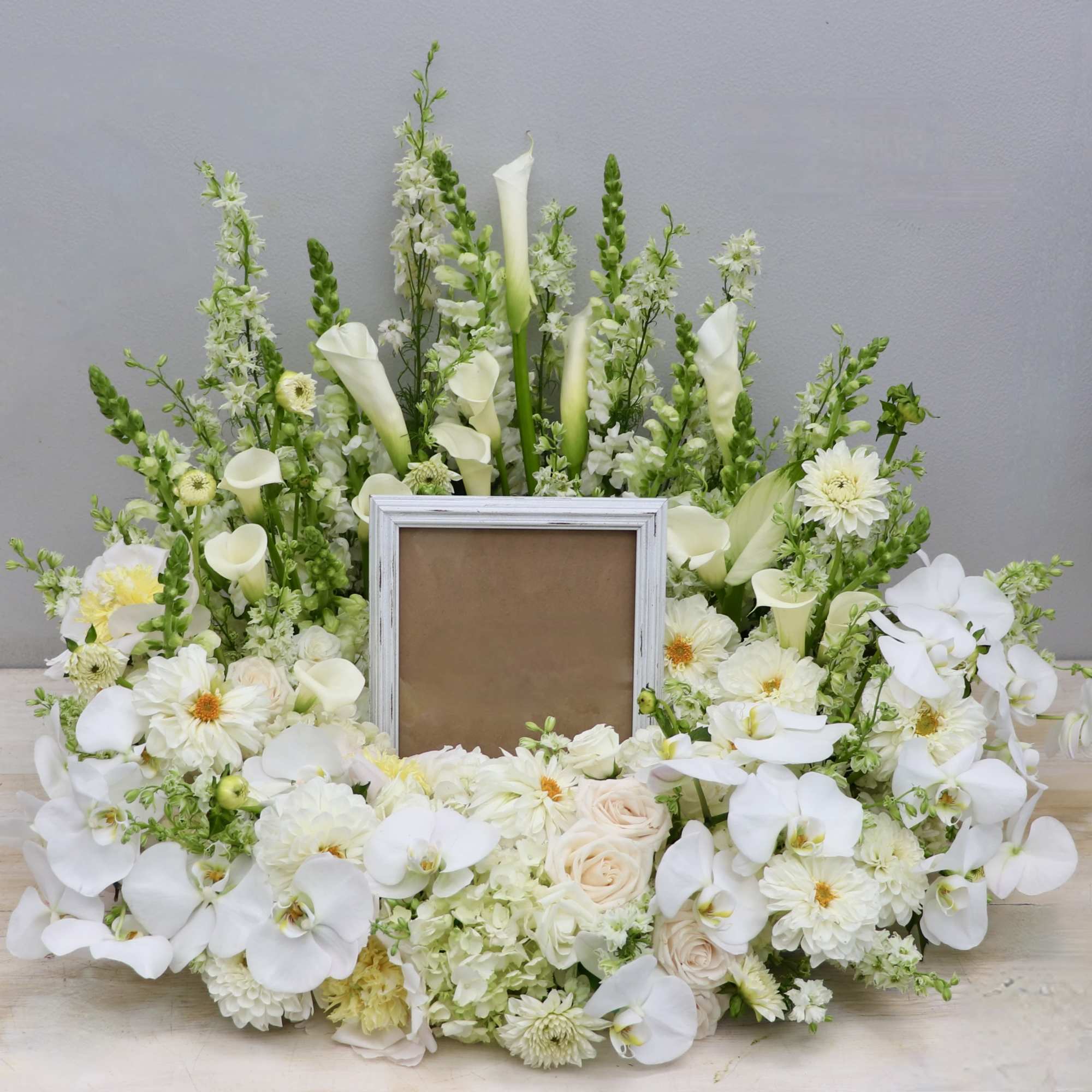 This urn tribute wreath includes a mix of orchids, roses, and seasonal