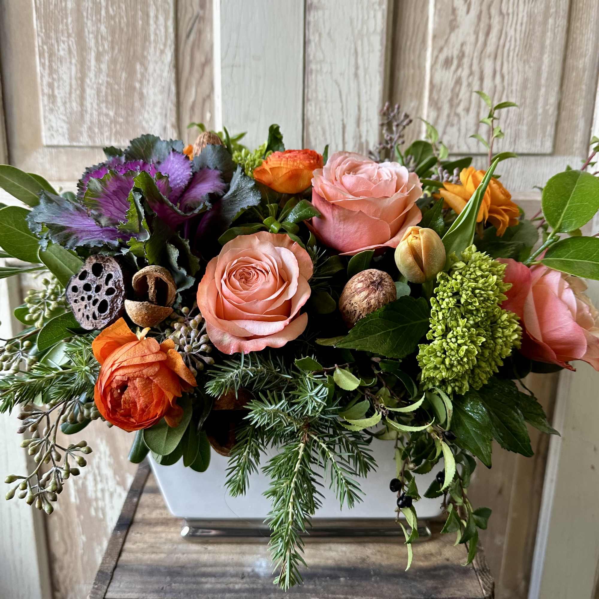 A seasonal display of kale, two toned orange roses, ranunculus and natural