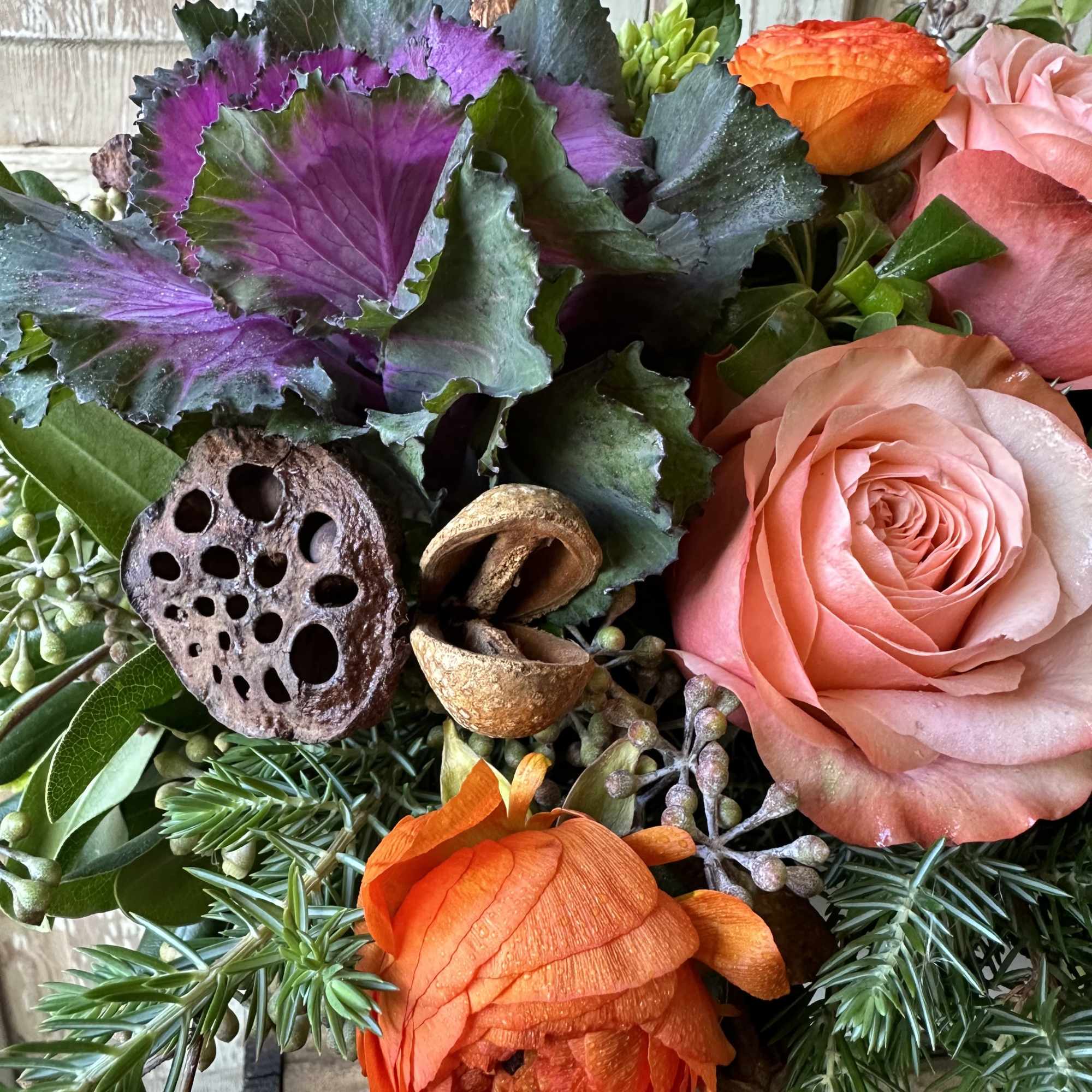 A seasonal display of kale, two toned orange roses, ranunculus and natural
