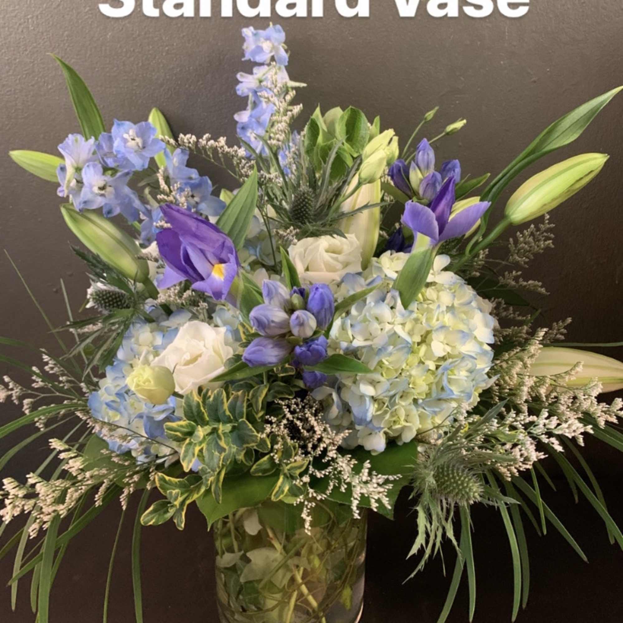 This arrangement contains delphinium, bells of ireland, lilies, hydrangea, blue iris, and