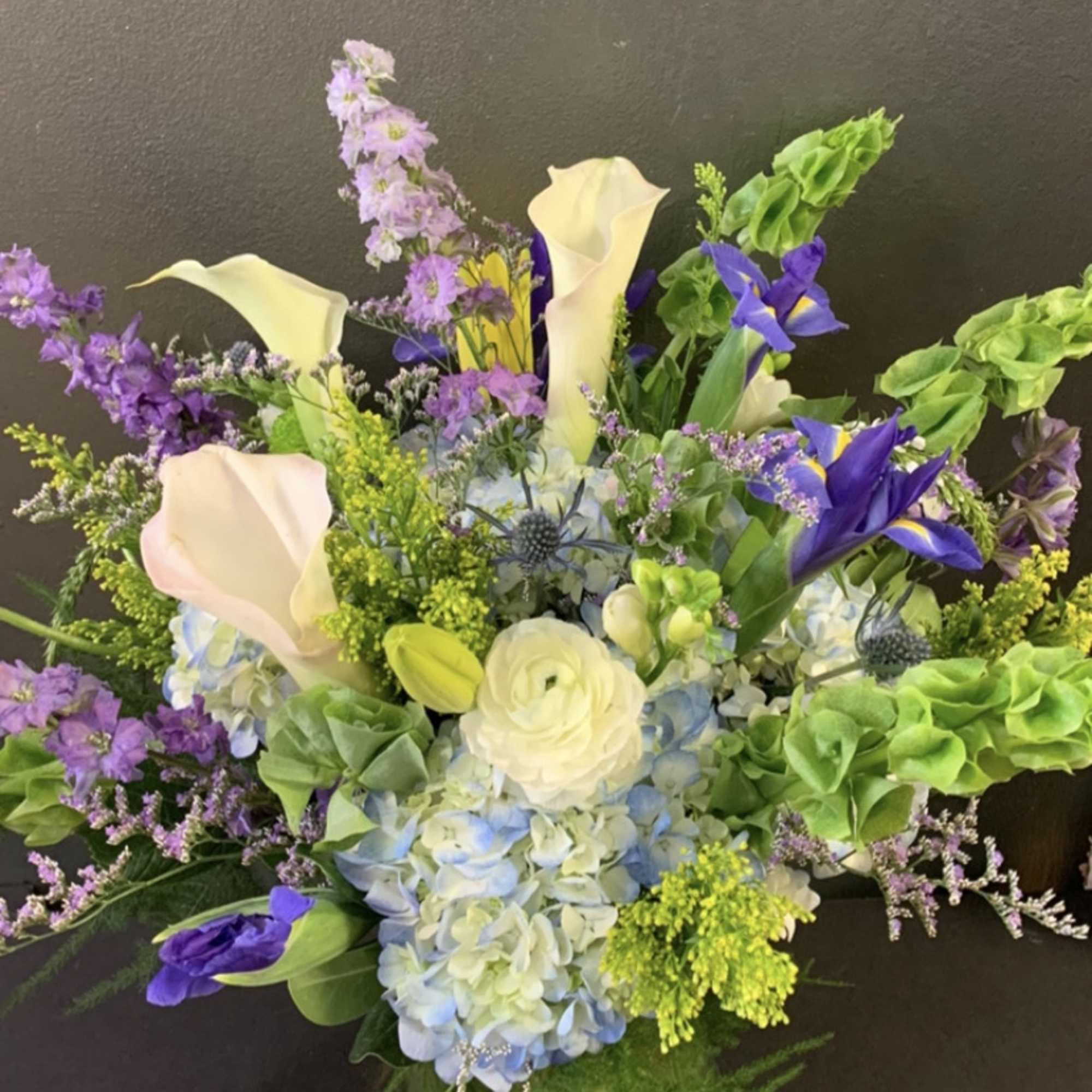 This arrangement contains delphinium, bells of ireland, lilies, hydrangea, blue iris, and