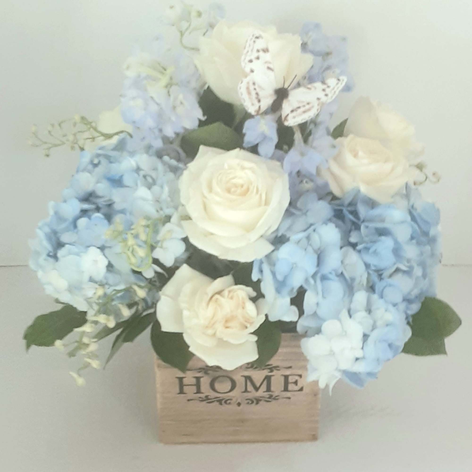 Arranged beautifully in a modern all wood cube,with white roses, blue delphinium