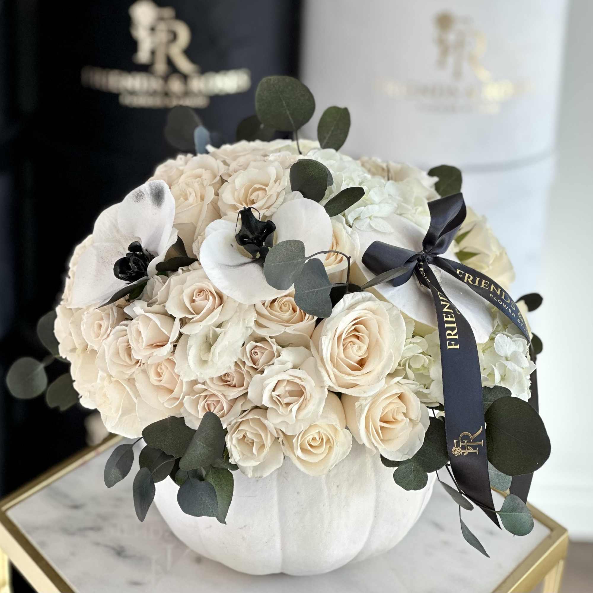 A chic floral arrangement in a white pumpkin, featuring white roses and