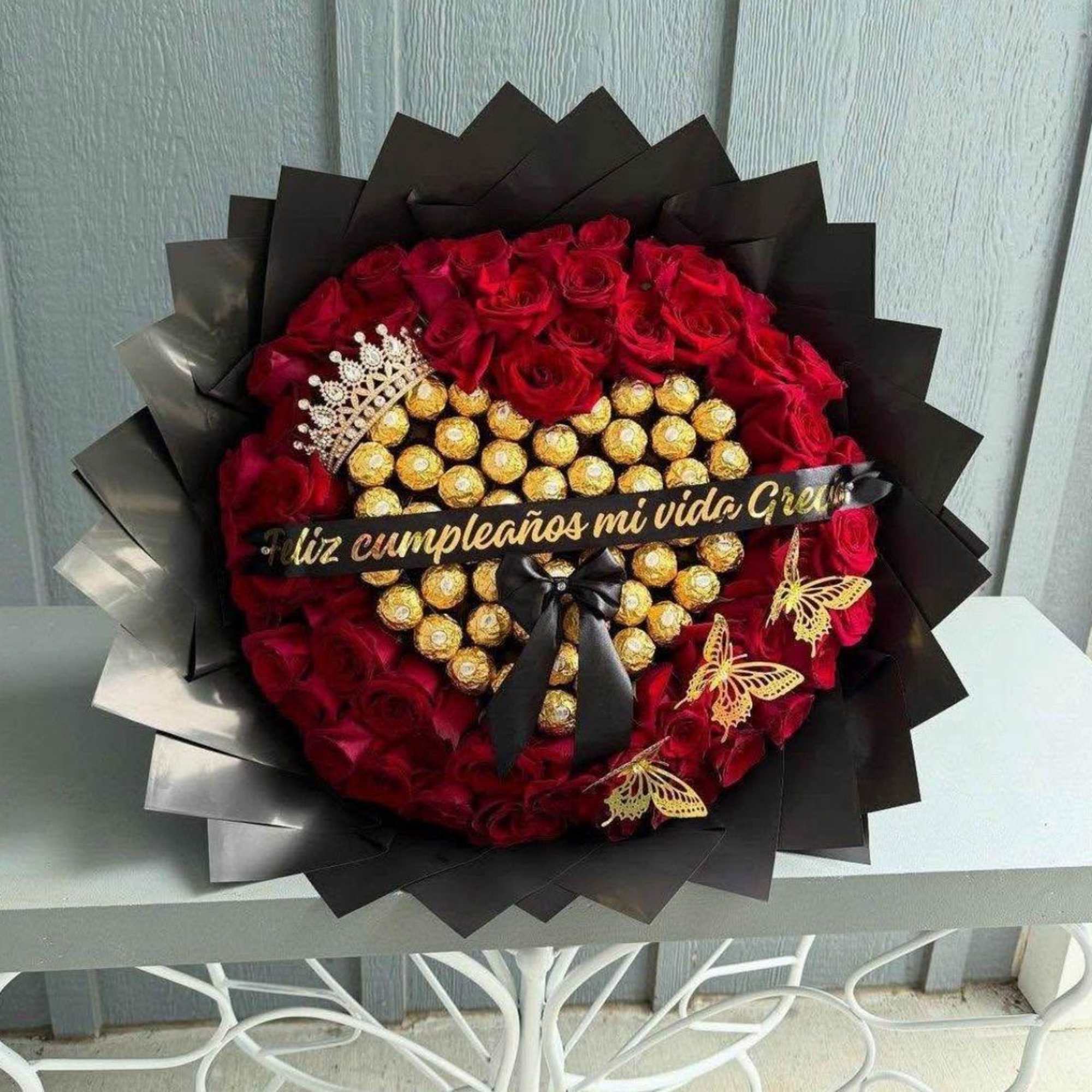 Buchon elaborado con rosas rojas, corona, liston, mariposas artificiales y chocolates ferrero.