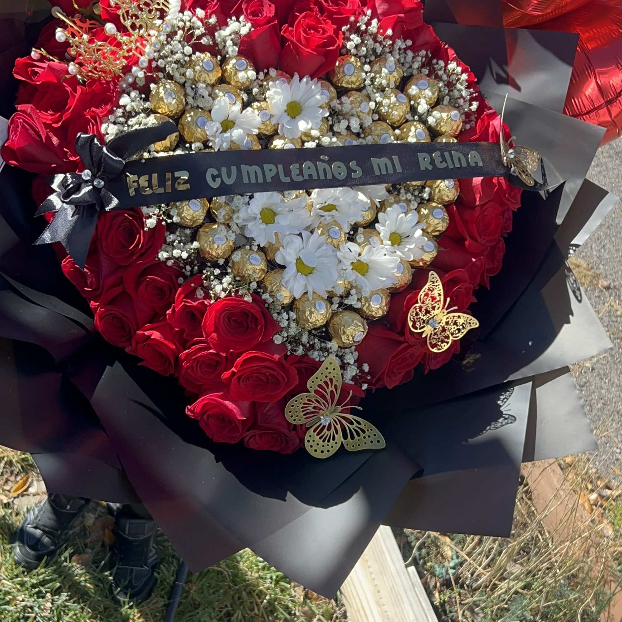 Buchon elaborado con rosas rojas, corona, liston, mariposas artificiales y chocolates ferrero.