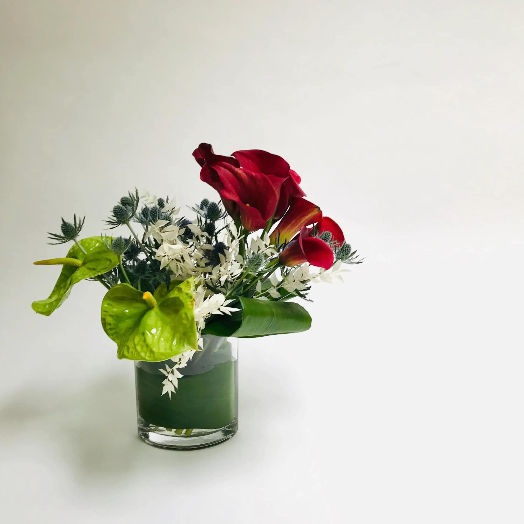 Comprised of bright orange red calla lilies, blues thistle and green Anthurium