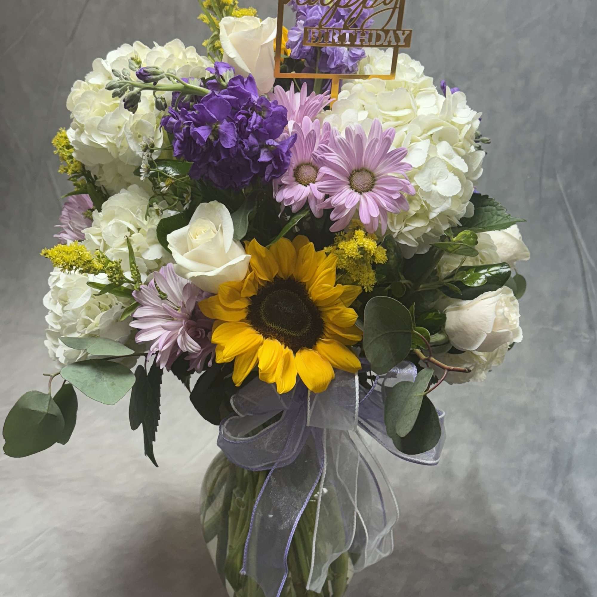 Golden sunflowers shine alongside white hydrangeas, roses, and cheerful daisies, accented with