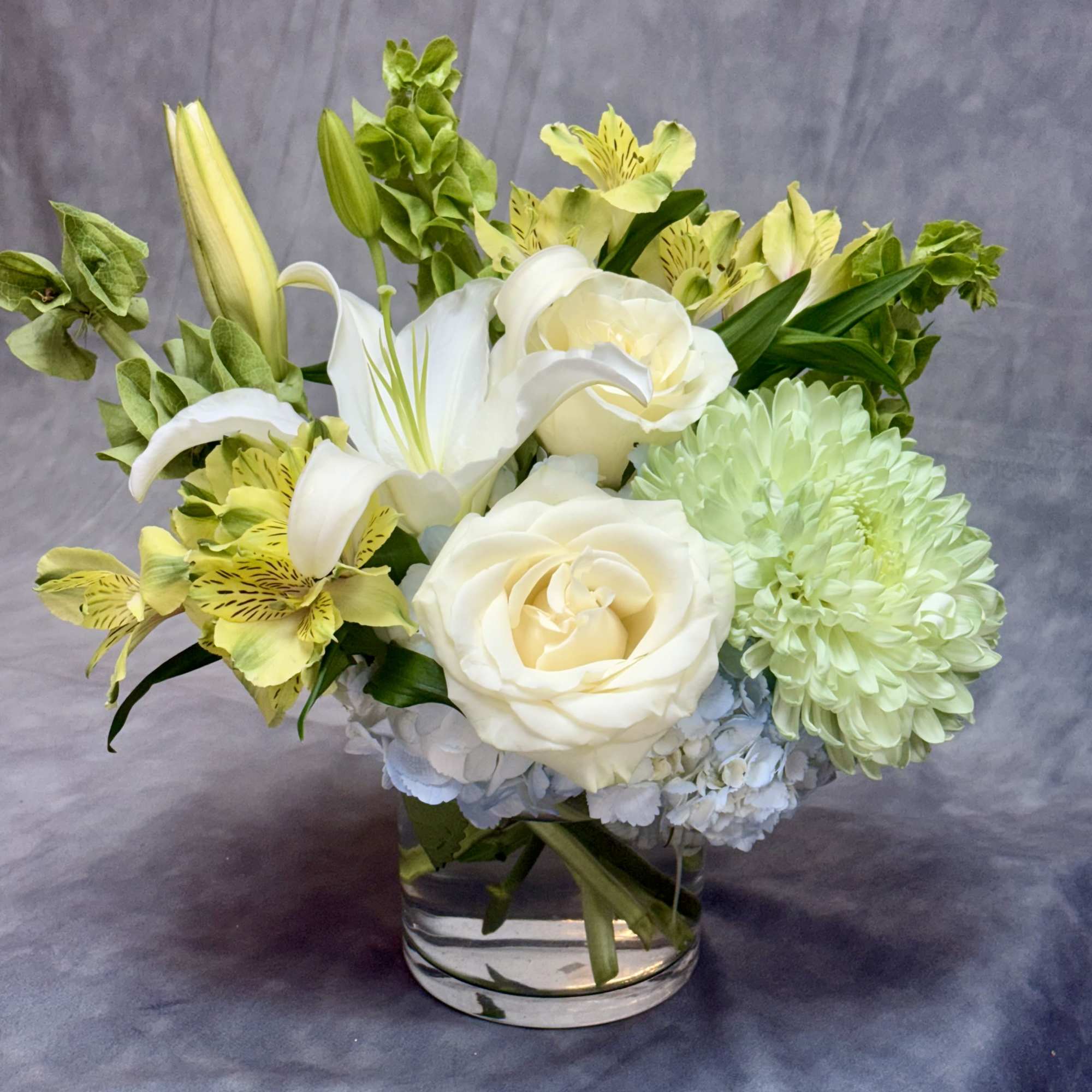 A graceful arrangement blending soft blue hydrangeas, elegant white lilies, creamy white