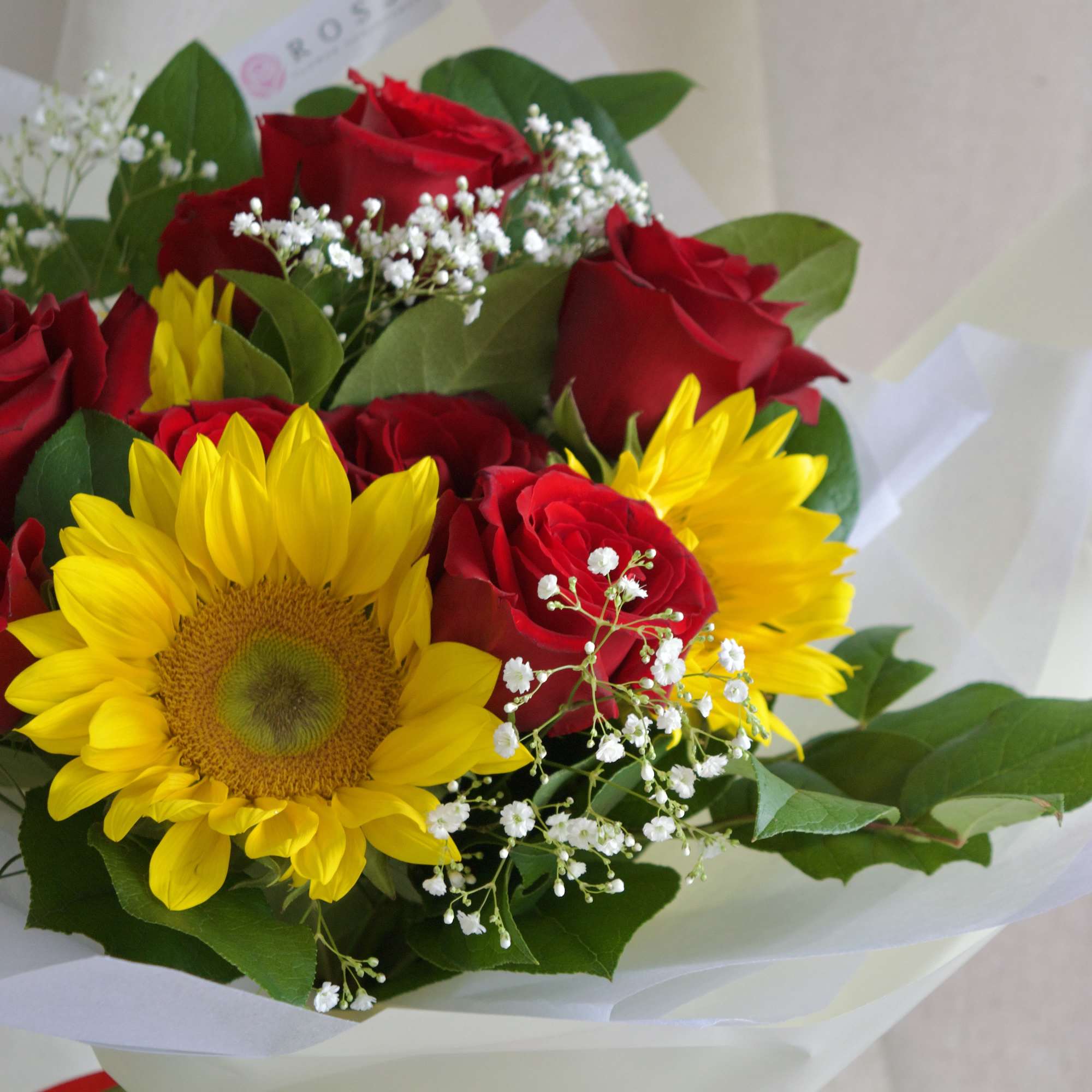 A round bouquet with red and yellow flowers, greenery, wrapped in pastel