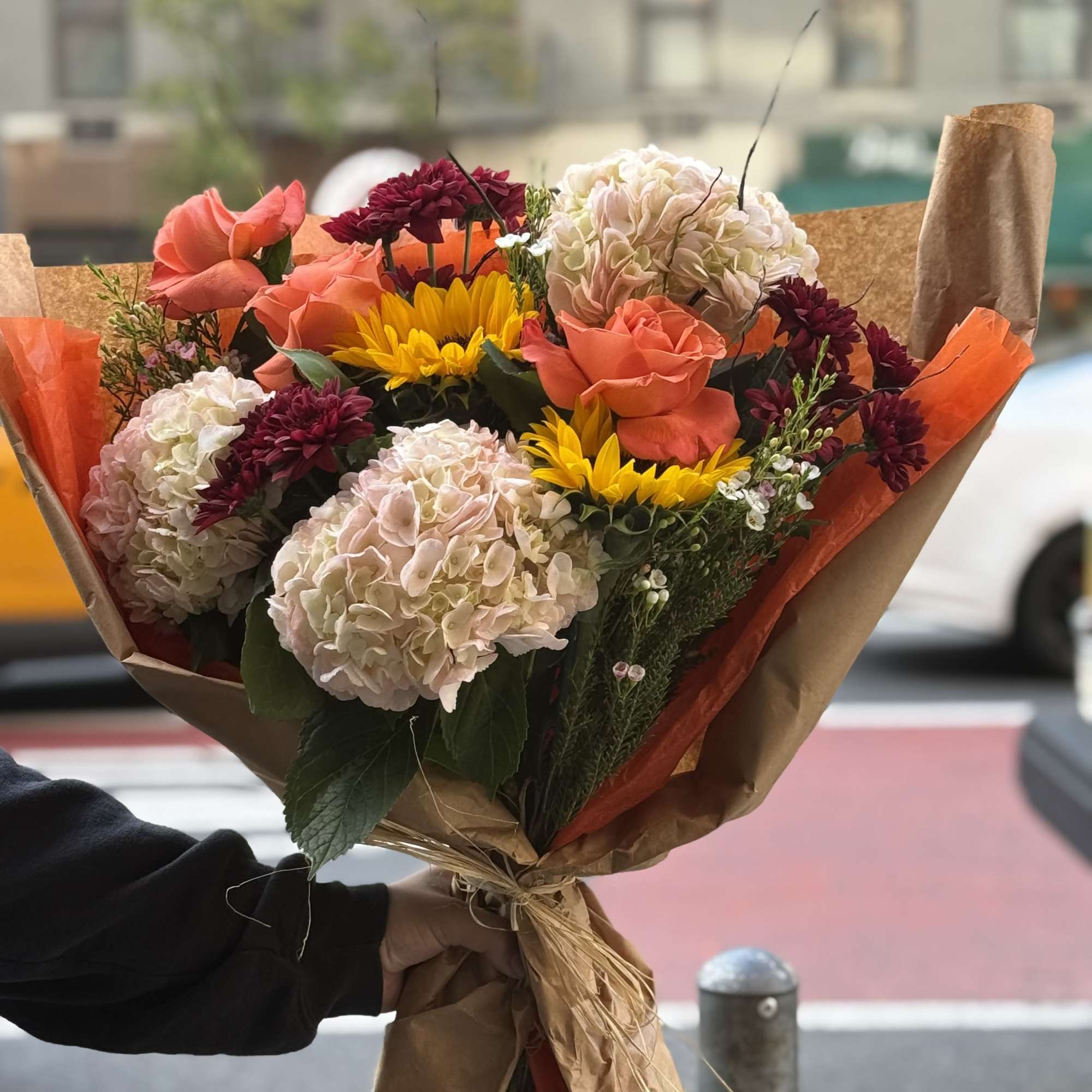 A warm and cheerful hand tied bouquet featuring vibrant oranges and sunny