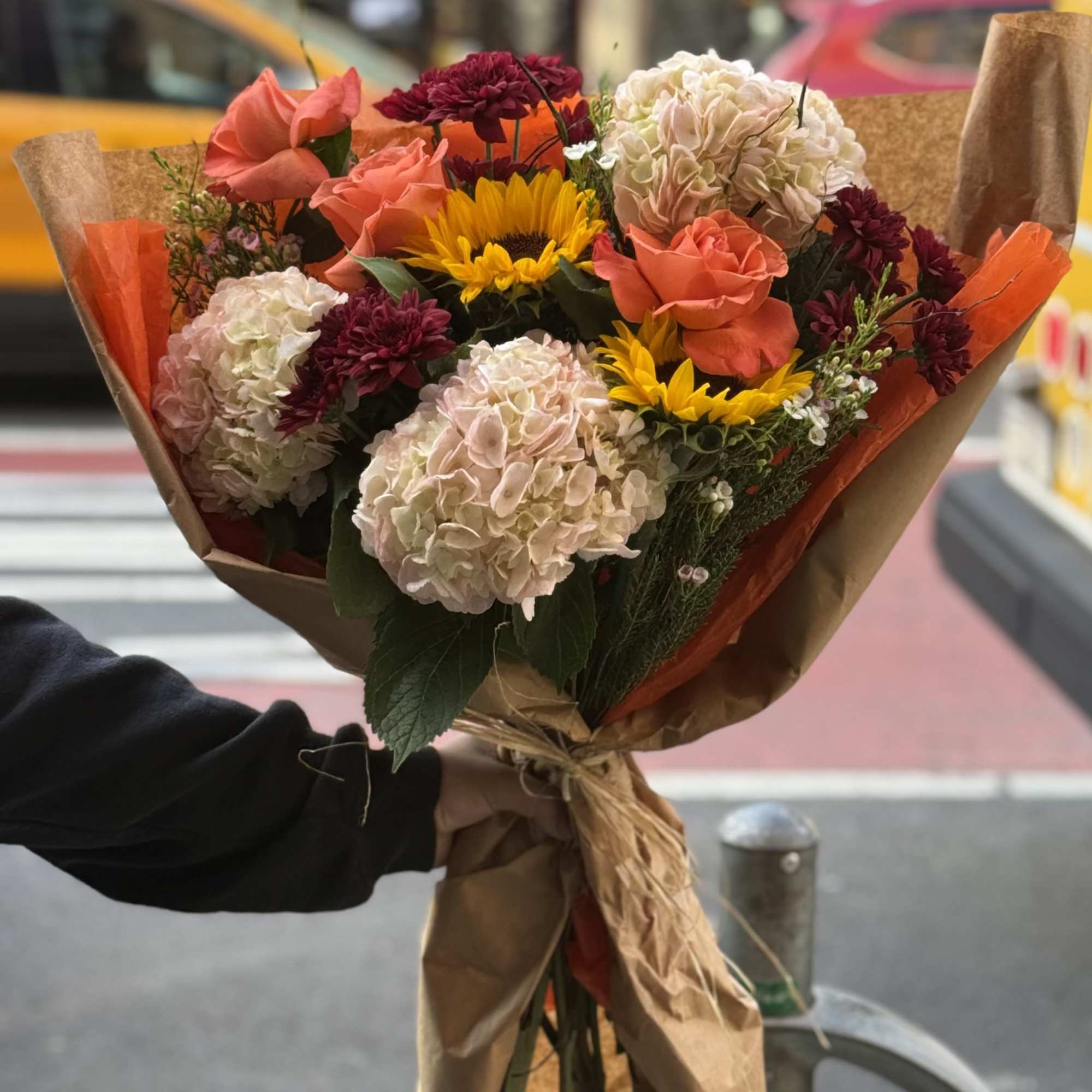 A warm and cheerful hand tied bouquet featuring vibrant oranges and sunny