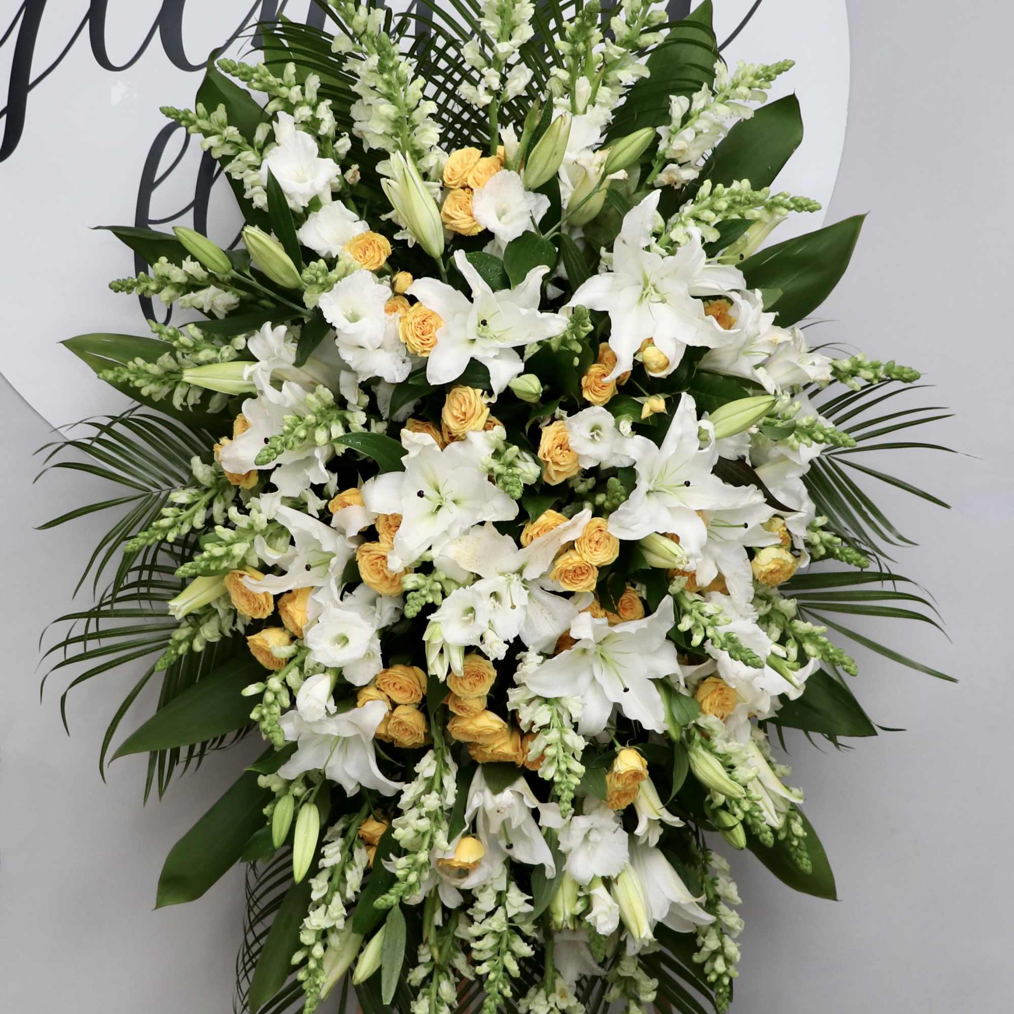 This sympathy spray includes bright yellow roses, stargazer lilies, and seasonal greens.