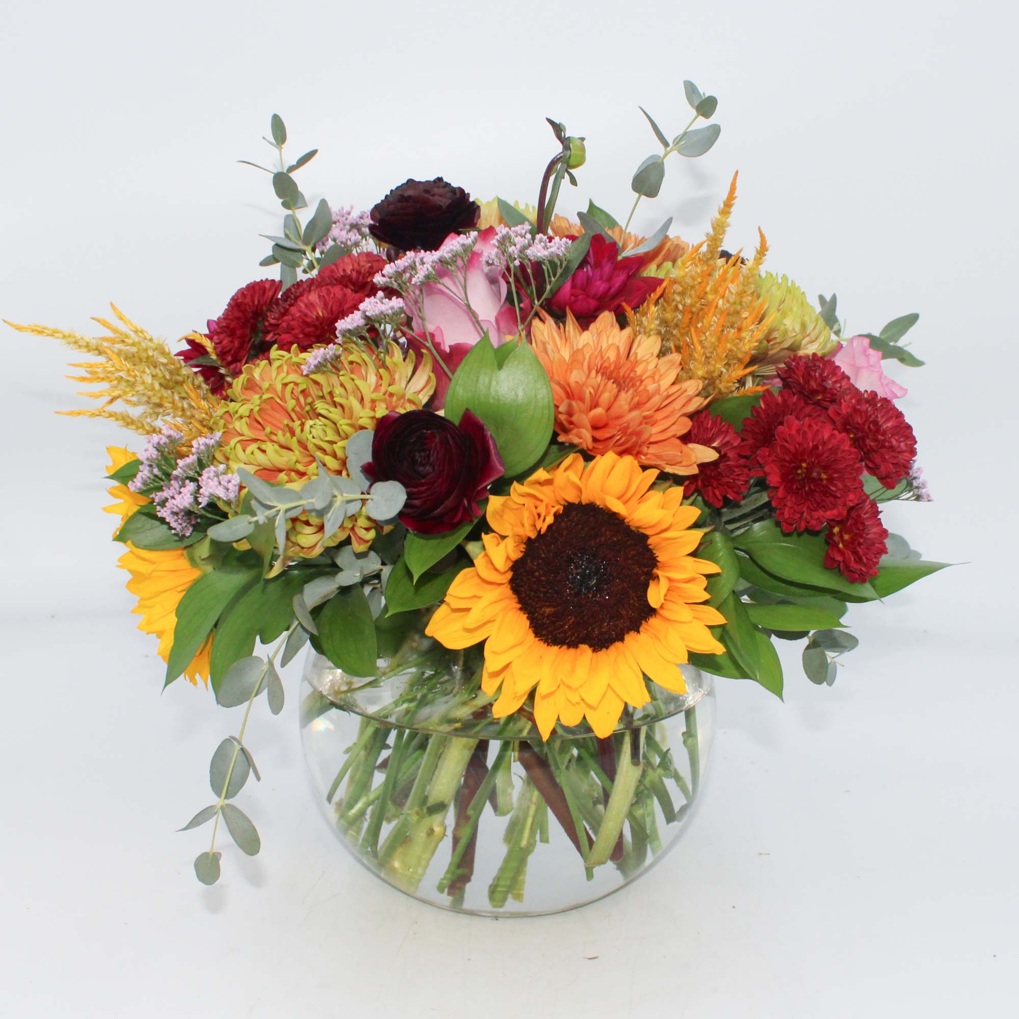Spiked Cider features Sunflowers, Burgundy Ranunculus, Deep Purple Roses, Burgundy Button Mums