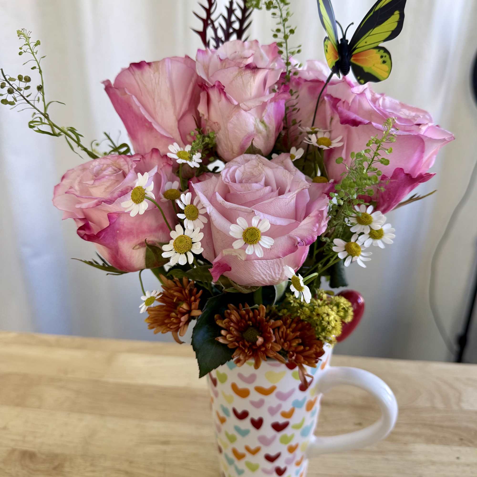 A delicate arrangement featuring soft pink roses, daisies, and wildflower accents in