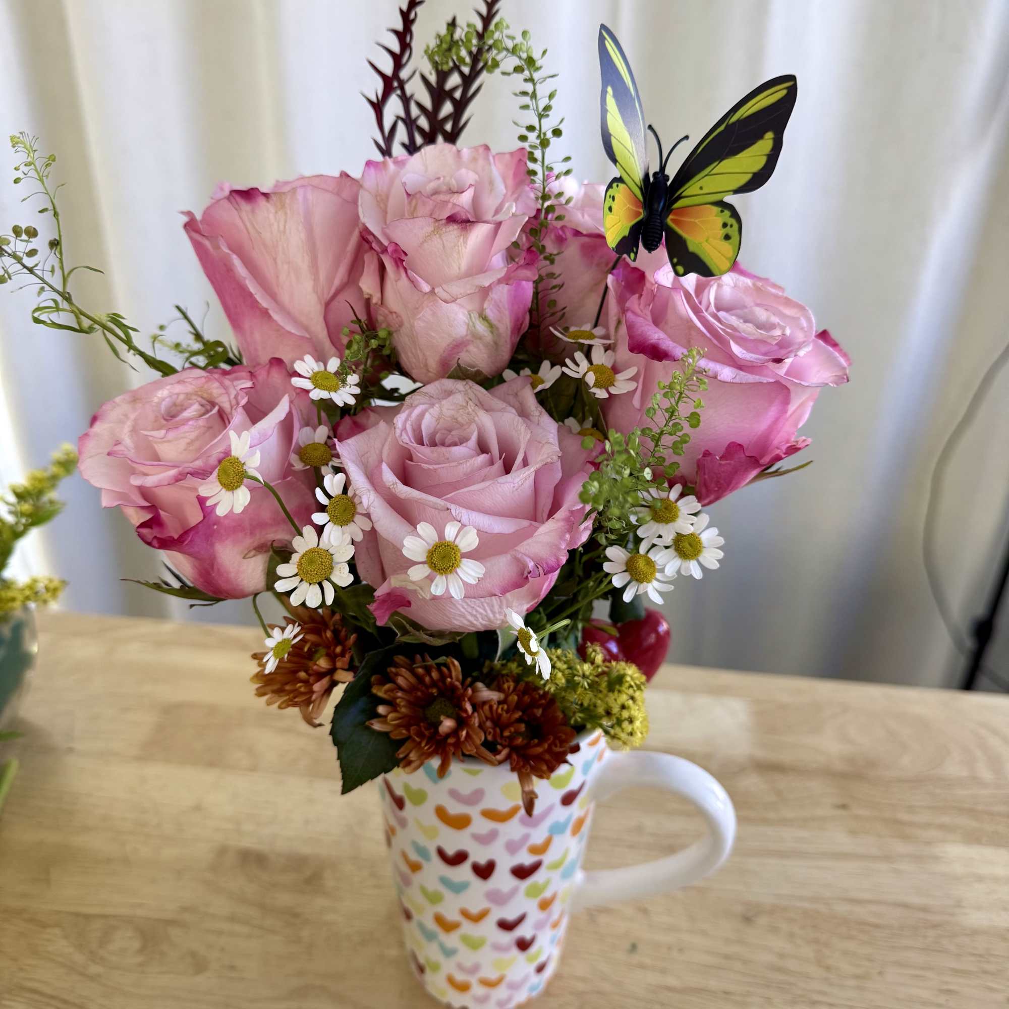 A delicate arrangement featuring soft pink roses, daisies, and wildflower accents in