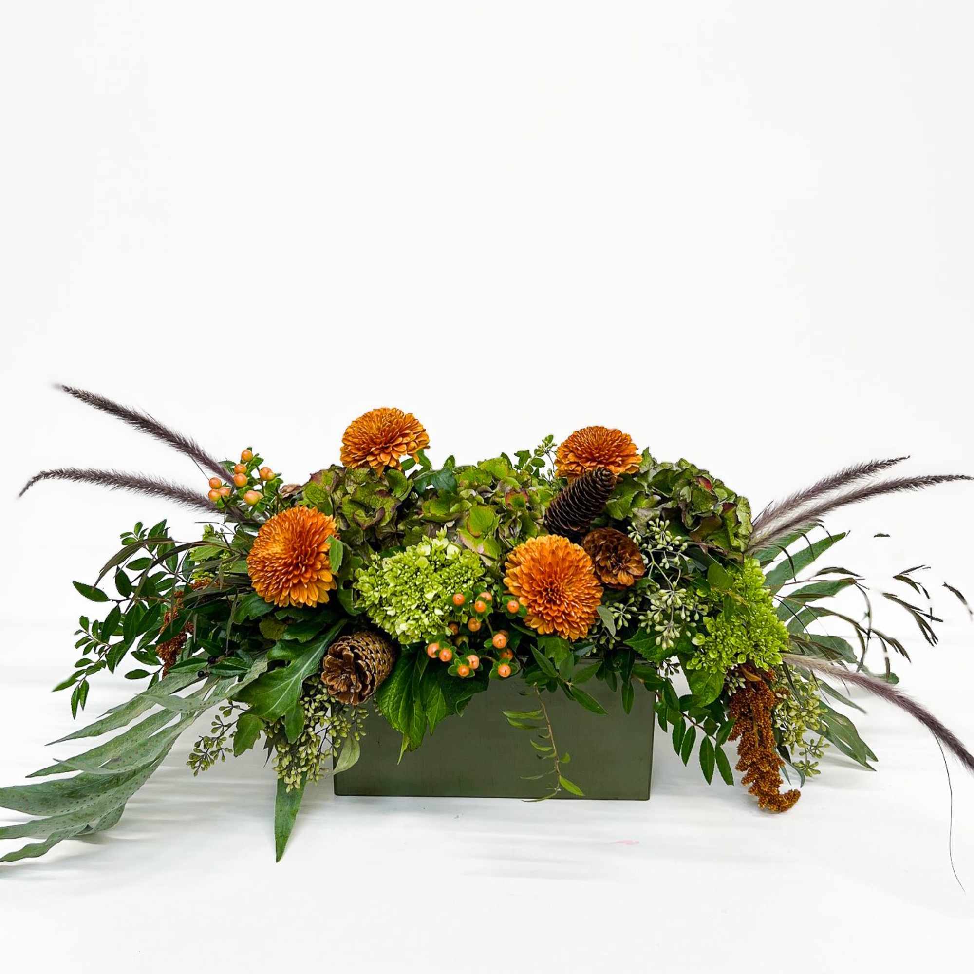 A long, low centerpiece blending antique hydrangeas, lush greenery, bronze-hued blooms, and