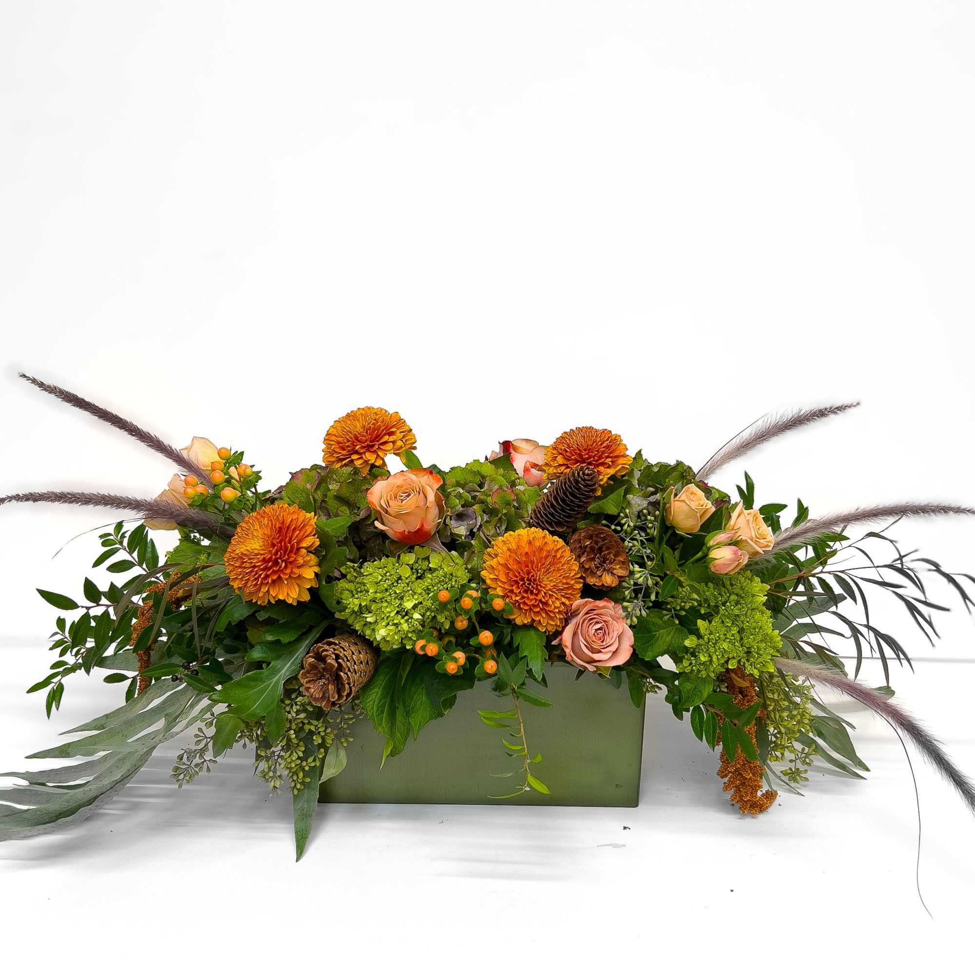 A long, low centerpiece blending antique hydrangeas, lush greenery, bronze-hued blooms, and