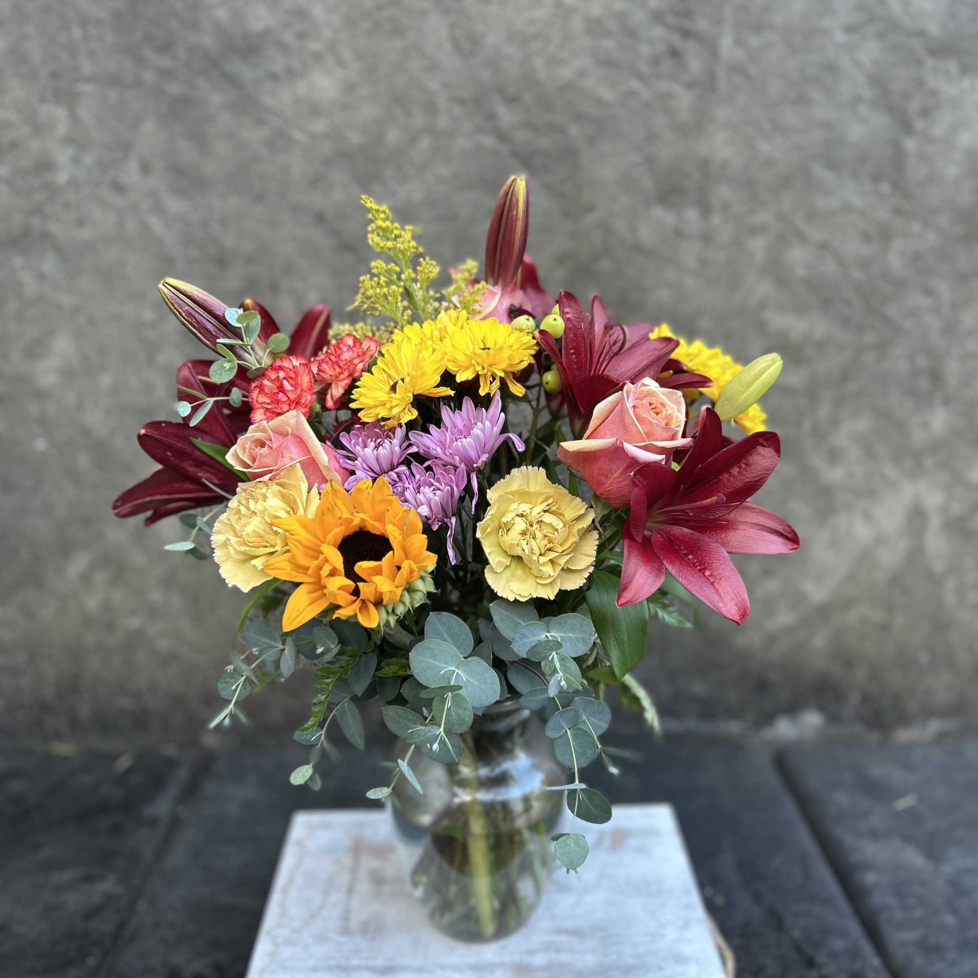 Burgundy Asiatic lilies, carnations, mini carnations, chrysanthemums, mini sunflower, sunflowers, roses, and