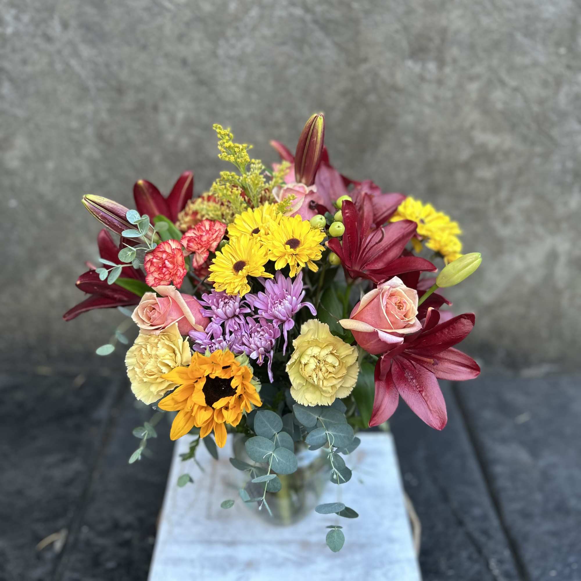 Burgundy Asiatic lilies, carnations, mini carnations, chrysanthemums, mini sunflower, sunflowers, roses, and