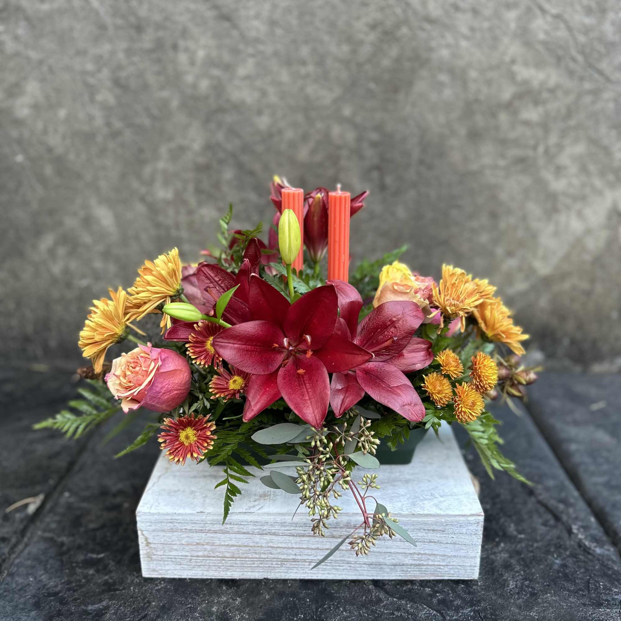 Burgundy Asiatic Lilies, roses, bronze chrysanthemums, daisies, seeded eucalyptus, two candles for