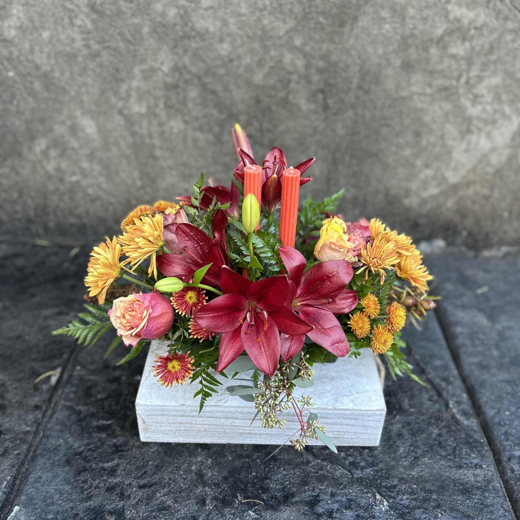 Burgundy Asiatic Lilies, roses, bronze chrysanthemums, daisies, seeded eucalyptus, two candles for