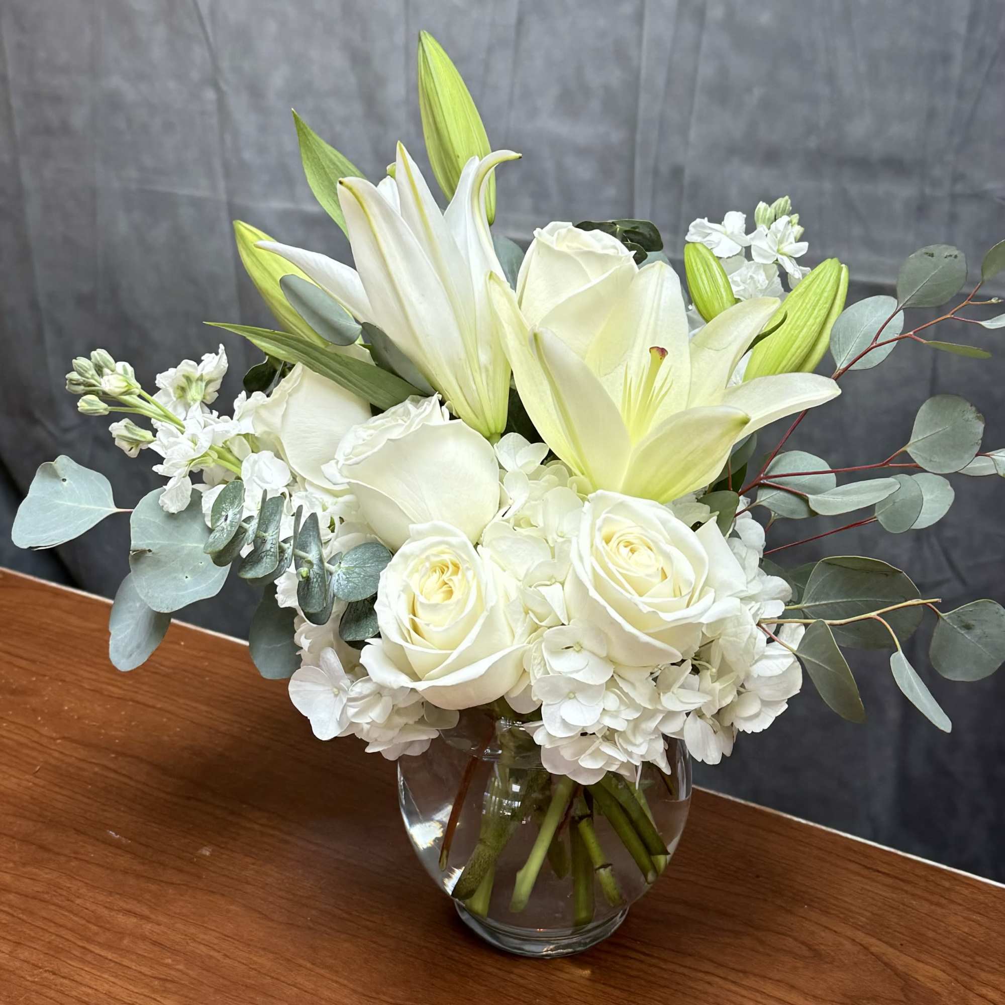 This arrangement includes white roses, white asiatic lilies, white stock, and dusty