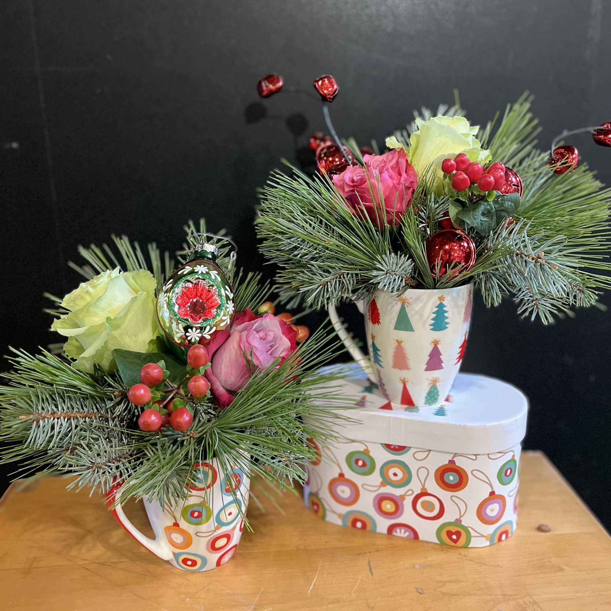 Holiday mugs are arranged with holiday greens and flowers. Holiday ornaments are