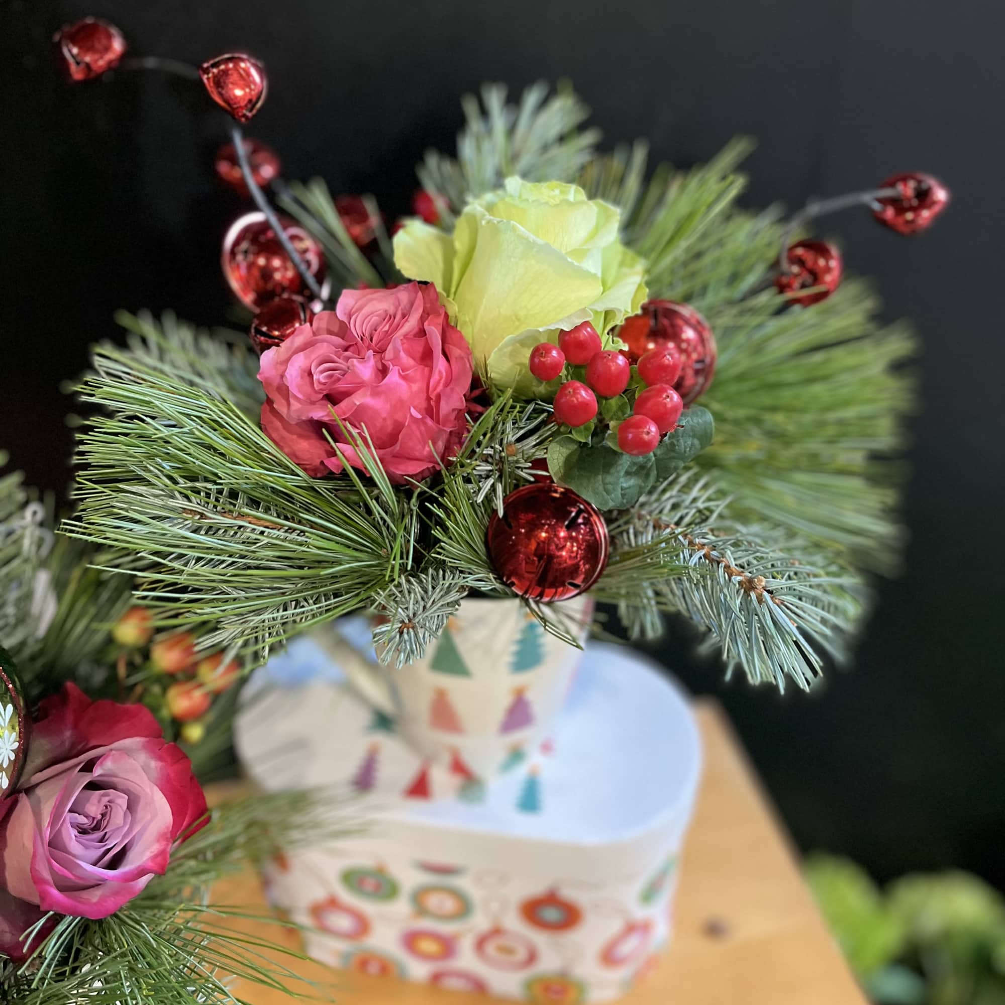 Holiday mugs are arranged with holiday greens and flowers. Holiday ornaments are