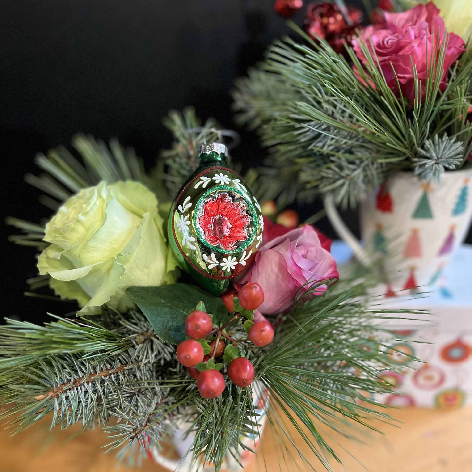 Holiday mugs are arranged with holiday greens and flowers. Holiday ornaments are
