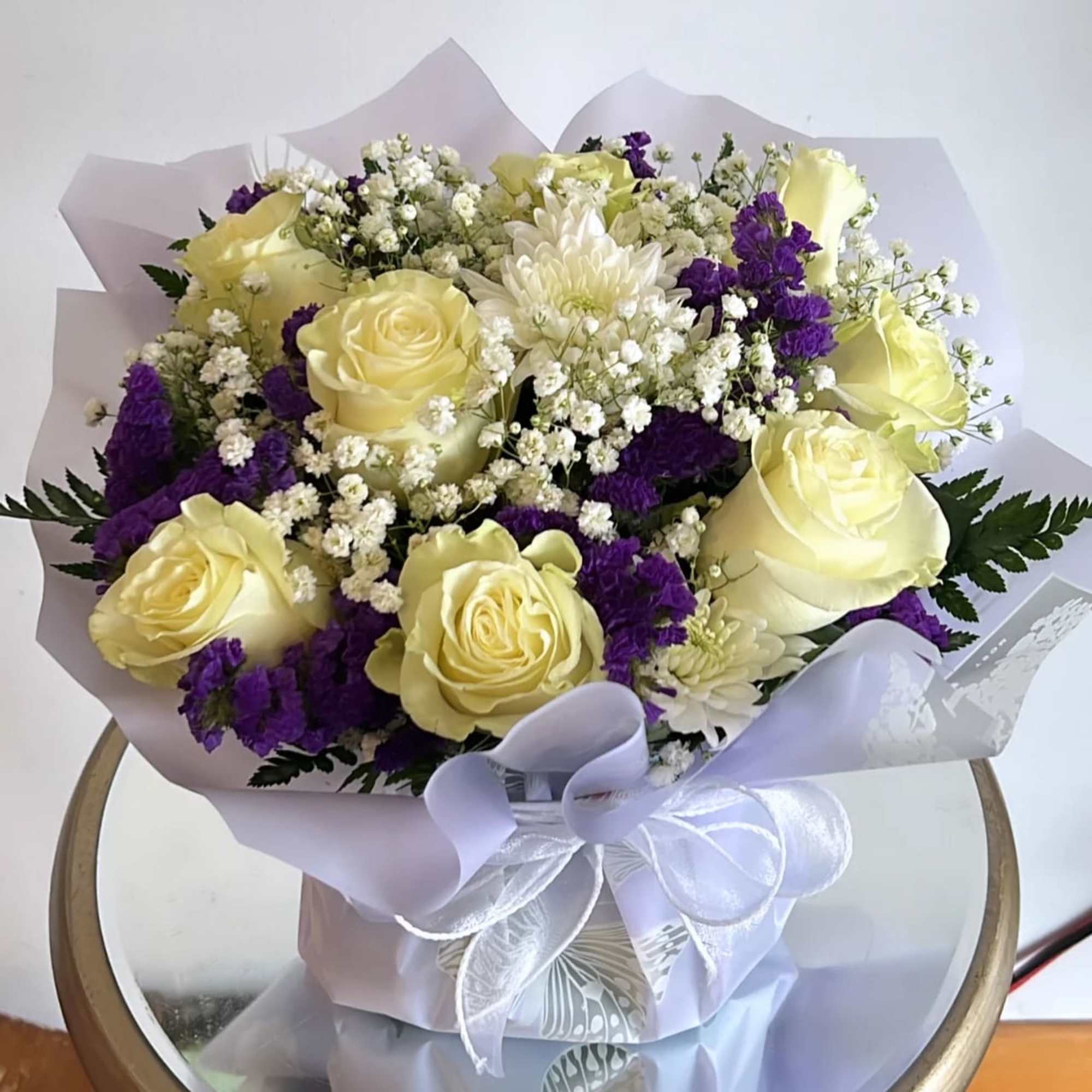 -The bouquet is composed primarily of delicate white roses, purple statice and