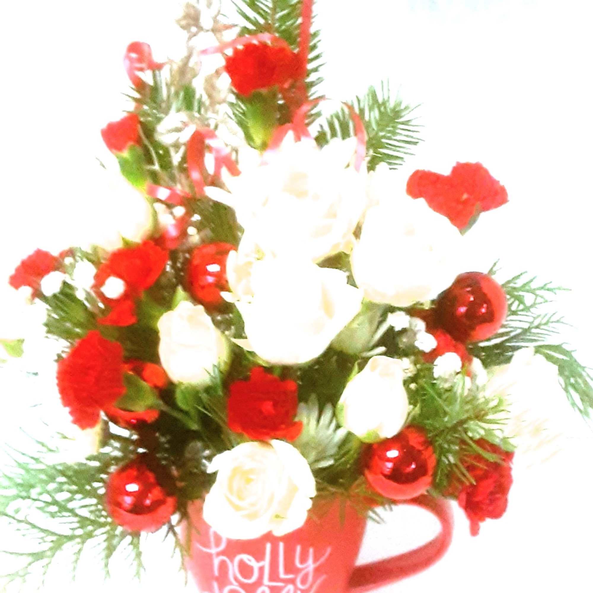 A holiday mug of miniature roses and carnations with holiday greenery, accented