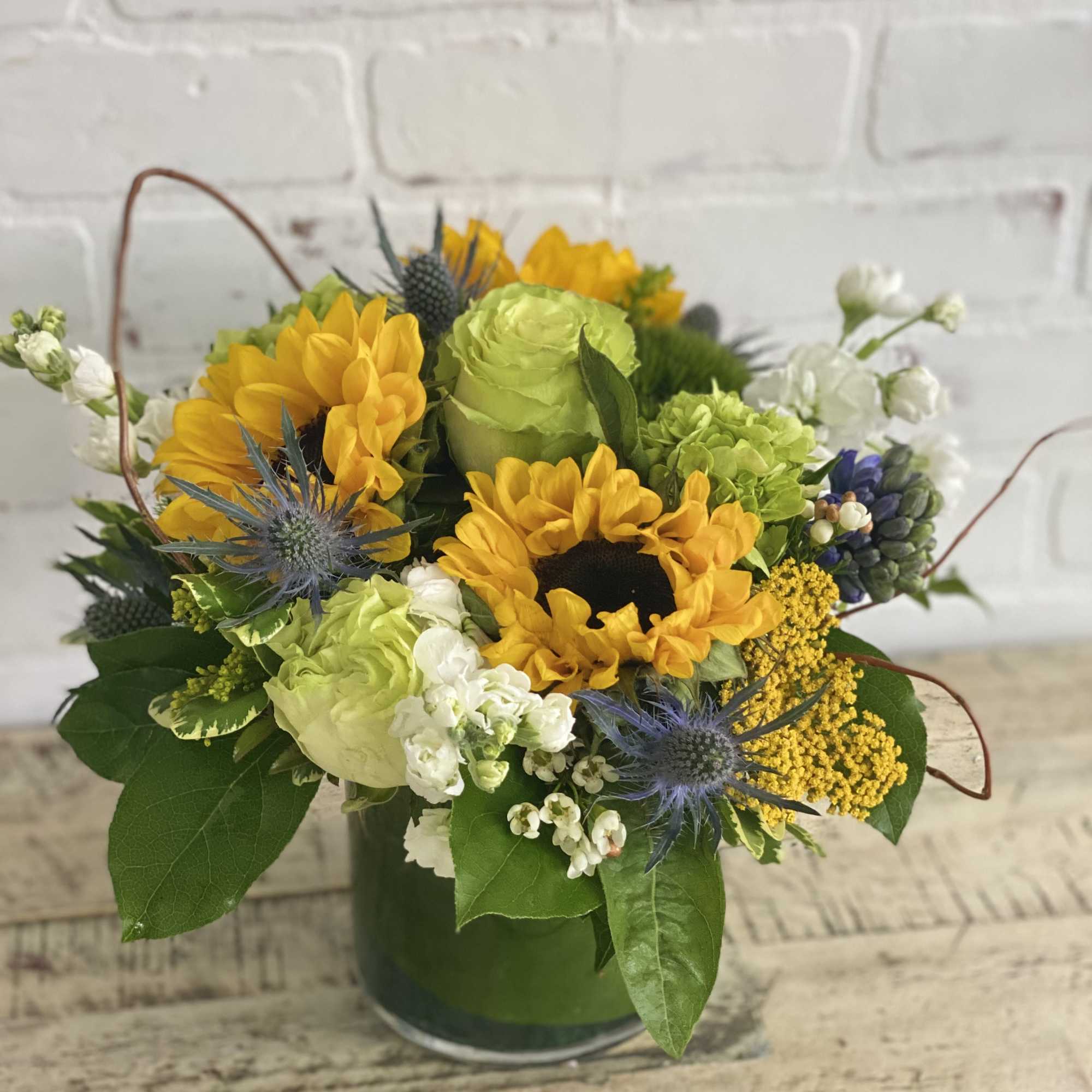 Cute arrangement of sunflowers and green blooms arranged in a 5x5 cylinder