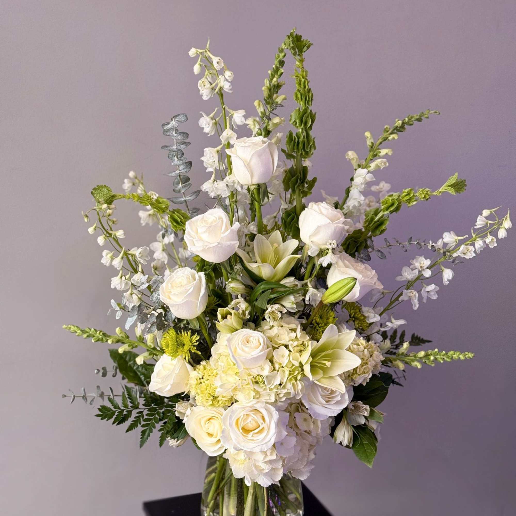 An arrangement of white florals and greens in a clear vase. (Inquire