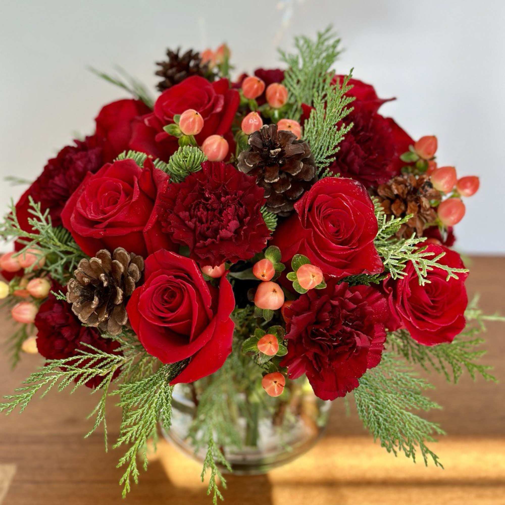 The winter flower arrangement features vibrant red roses and carnations accented with