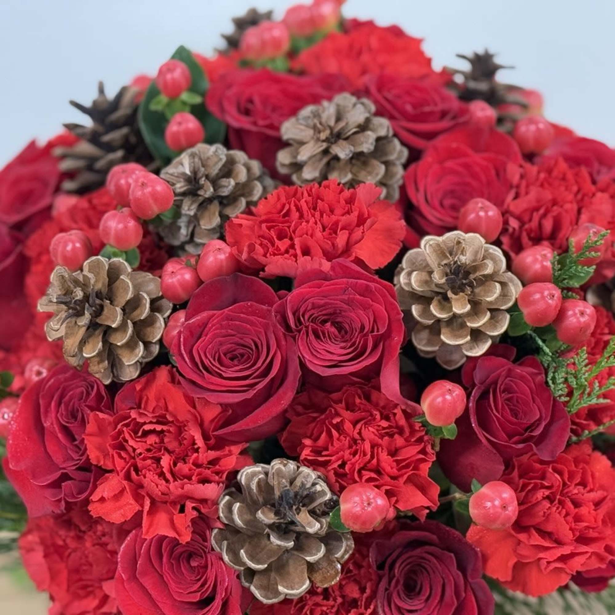 The winter flower arrangement features vibrant red roses and carnations accented with