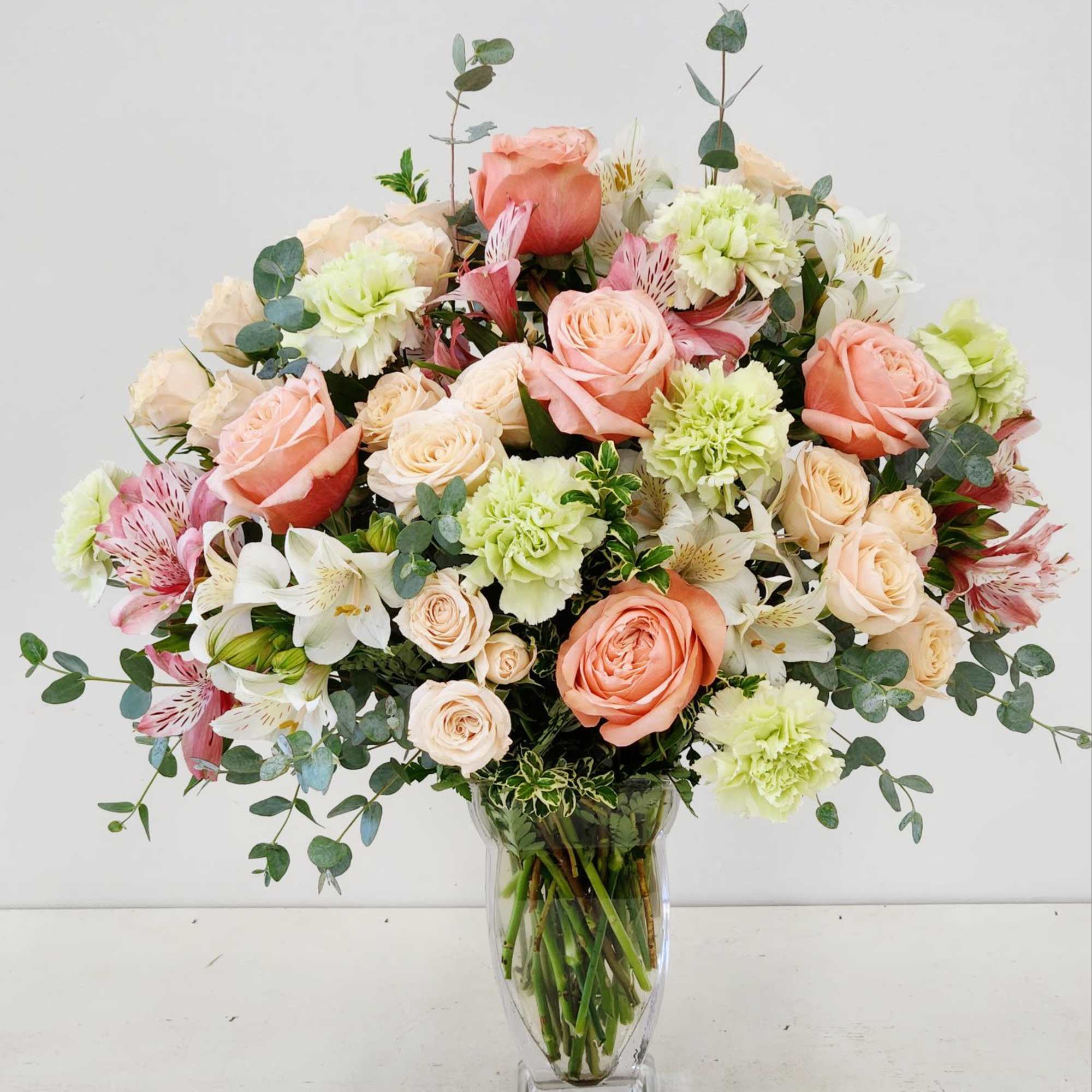 Soft peach roses and green carnations blend seamlessly with delicate peach spray