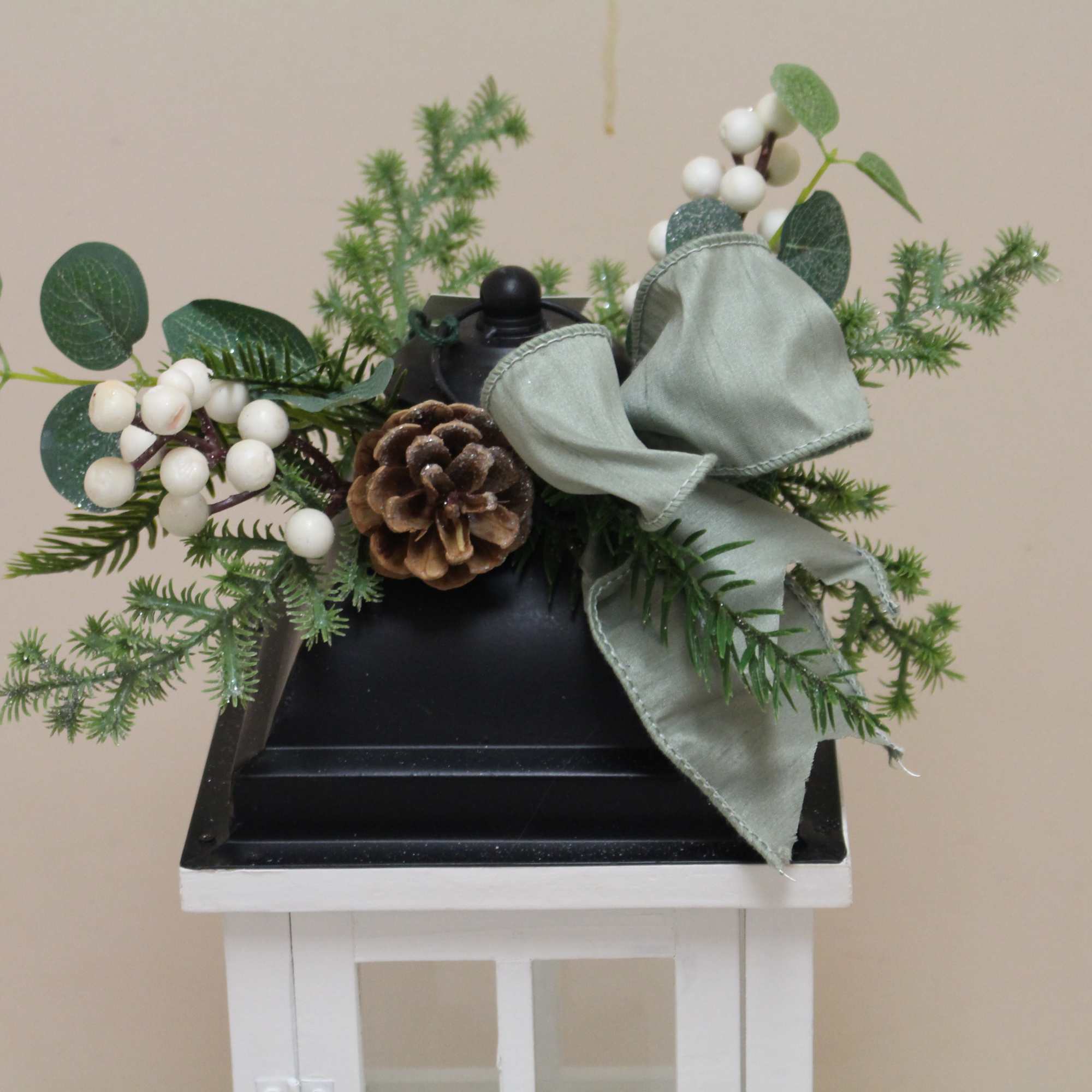 A white lantern with a metal black top adorned with a wintergreen