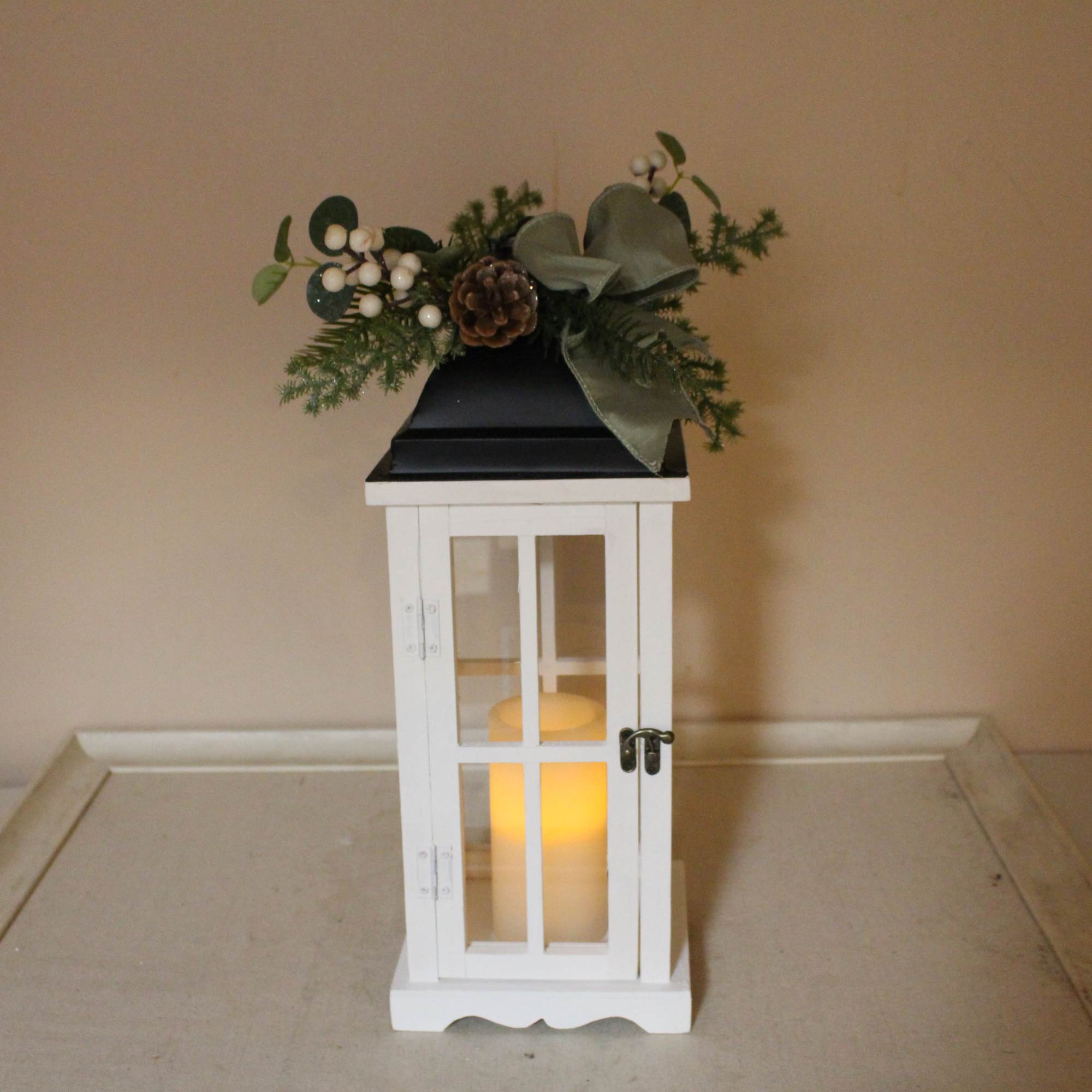 A white lantern with a metal black top adorned with a wintergreen