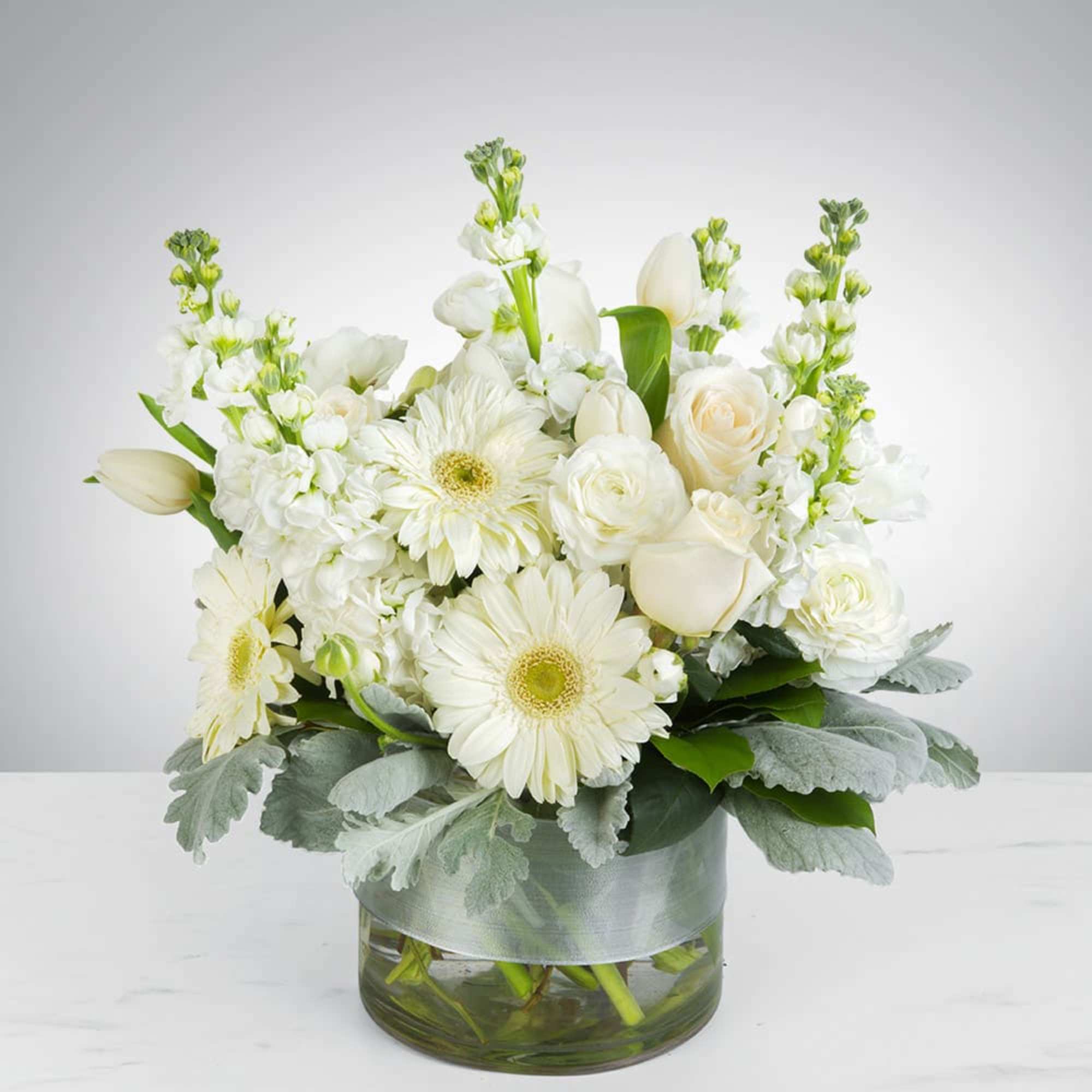 This arrangement contains gerbera daisies, roses, stock, and other seasonal blooms. 