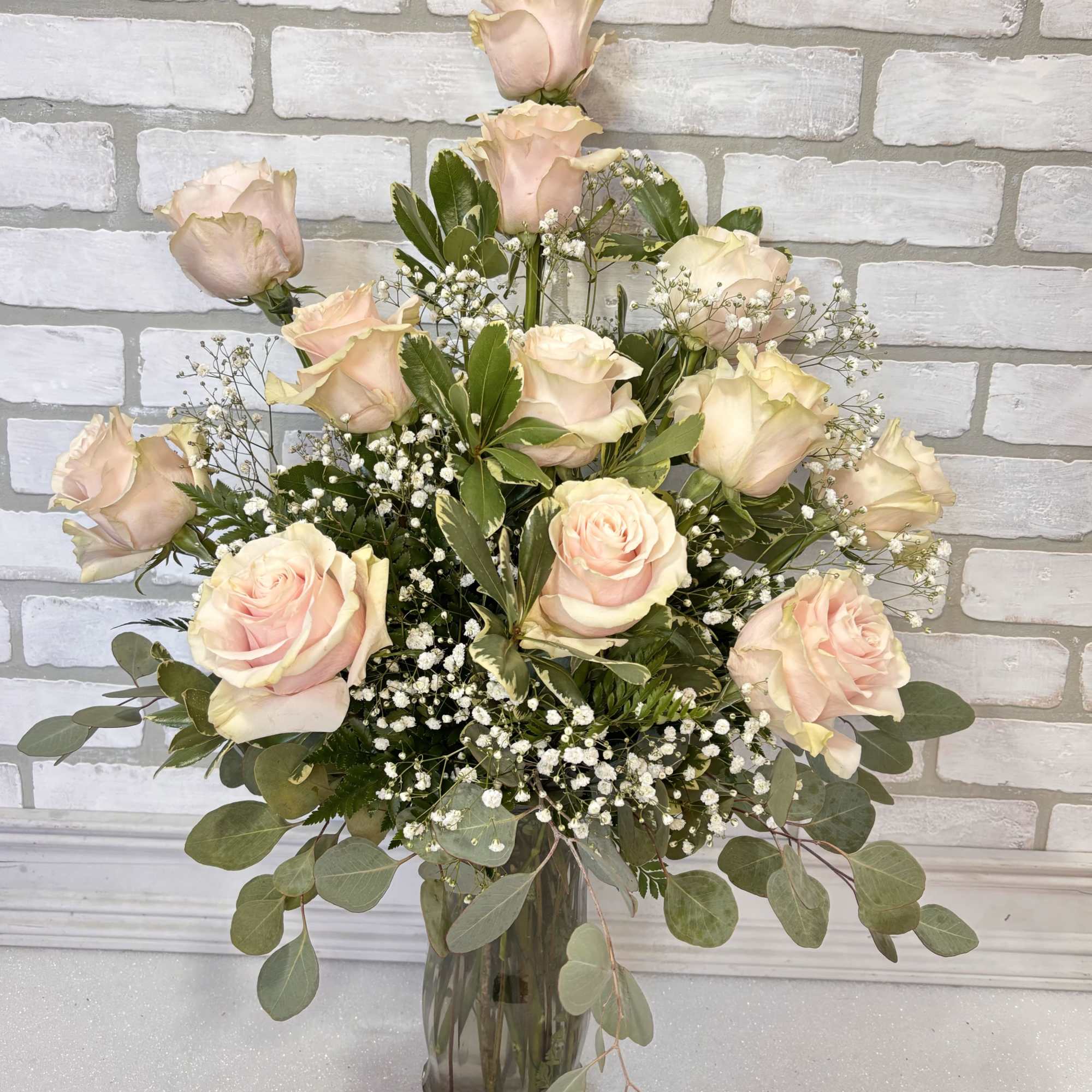 12 beautiful light pink roses arranged in a glass vase. 
