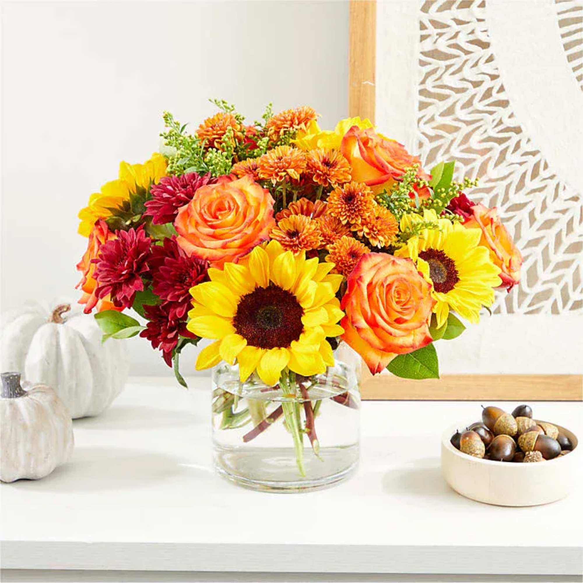 A vivid blend of sunflowers, sunset-orange roses, and berry accents rises like