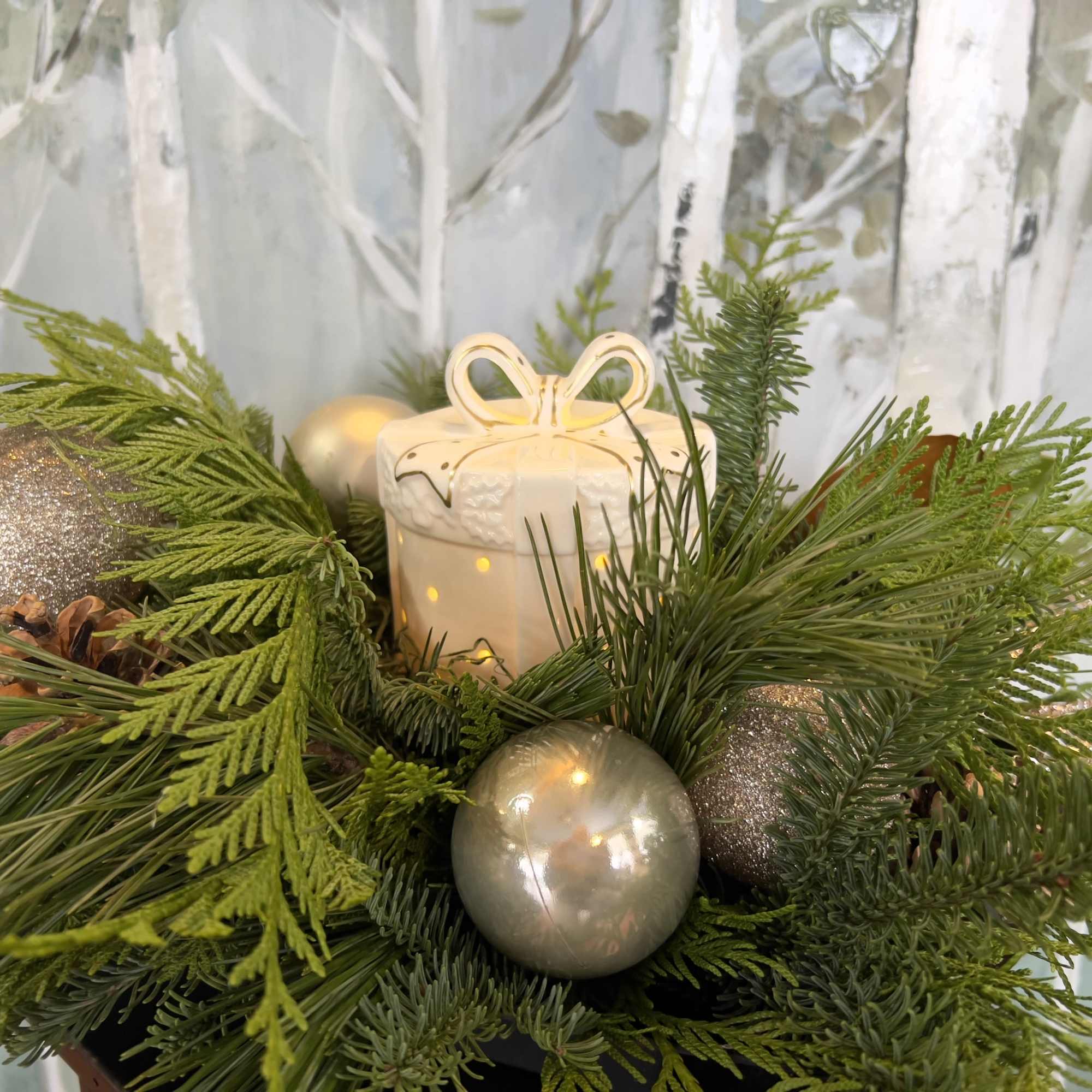 This arrangement incorporates a ceramic holiday present with a soft warm glow