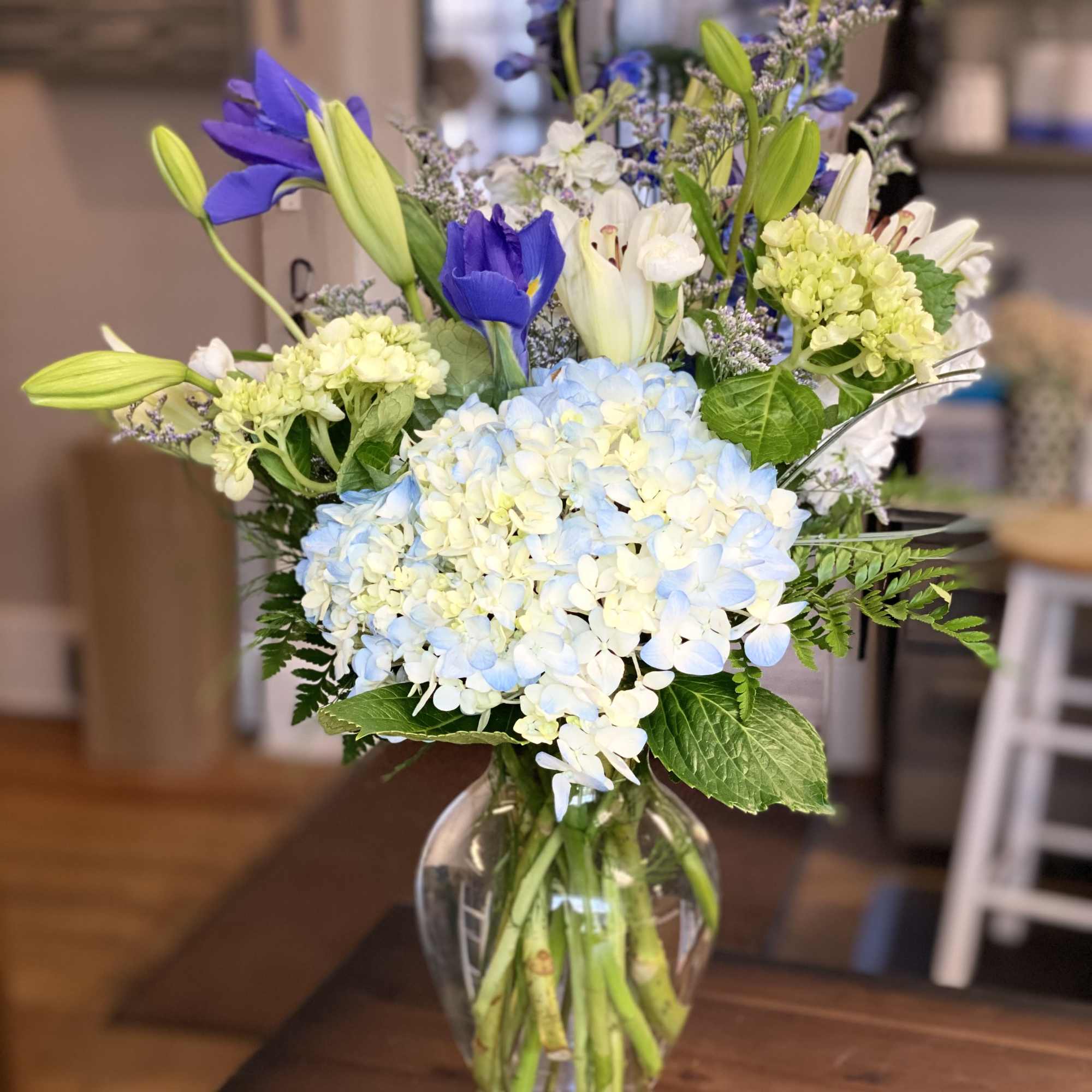 This arrangement contains delphinium, bells of ireland, asiatic lilies, hydrangea, blue iris