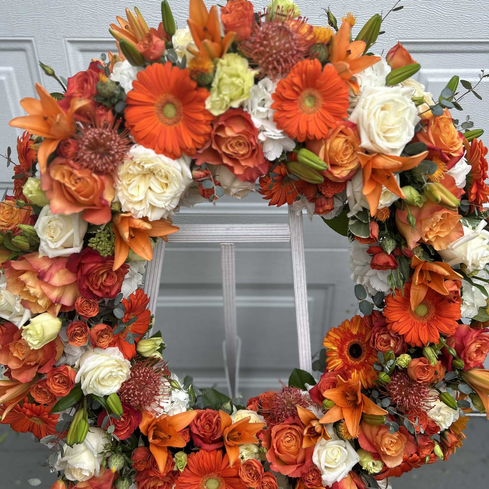 This orange wreath includes daisies, roses, and lilies to create a beautiful