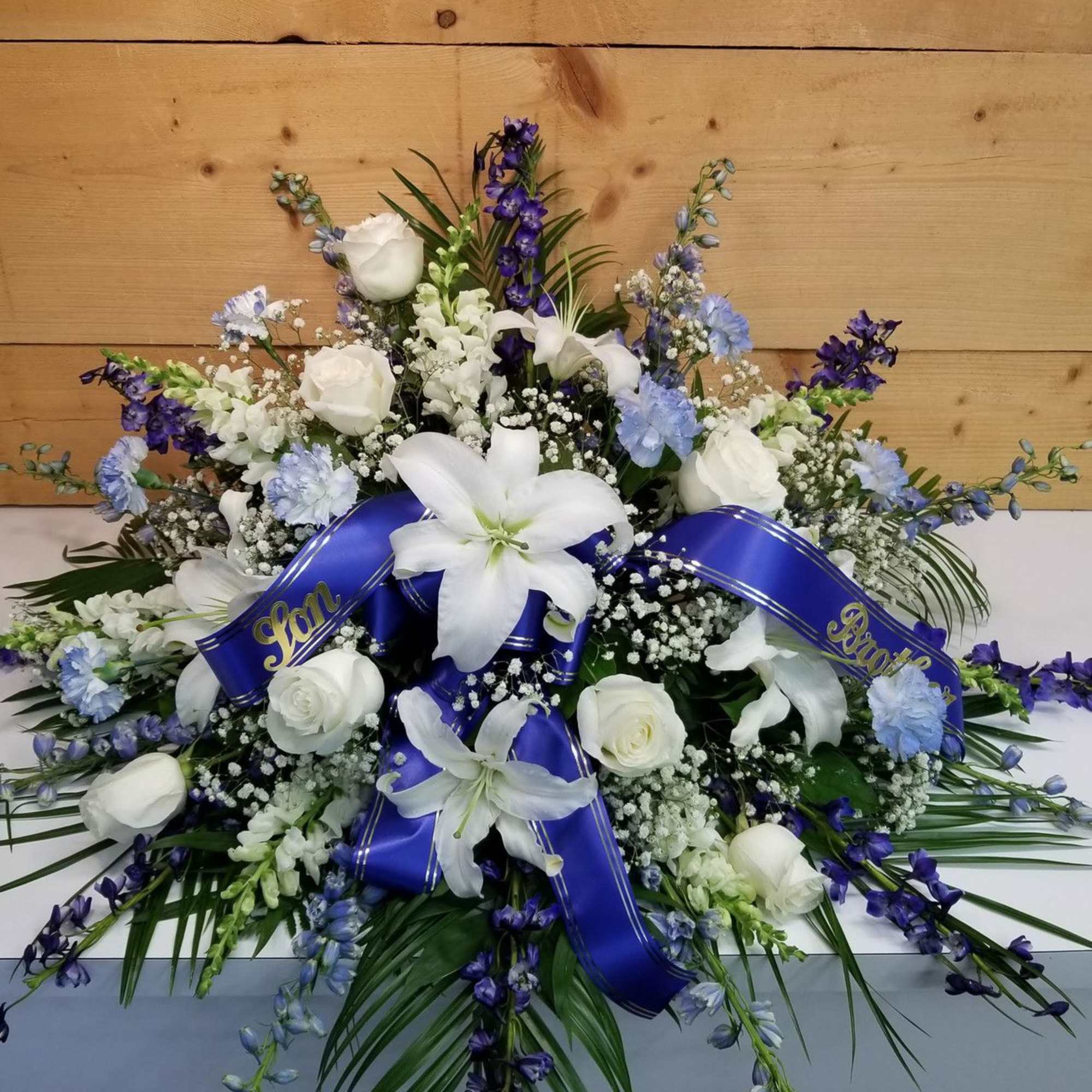 A stunning blue and white themed half casket spray featuring roses, lilies