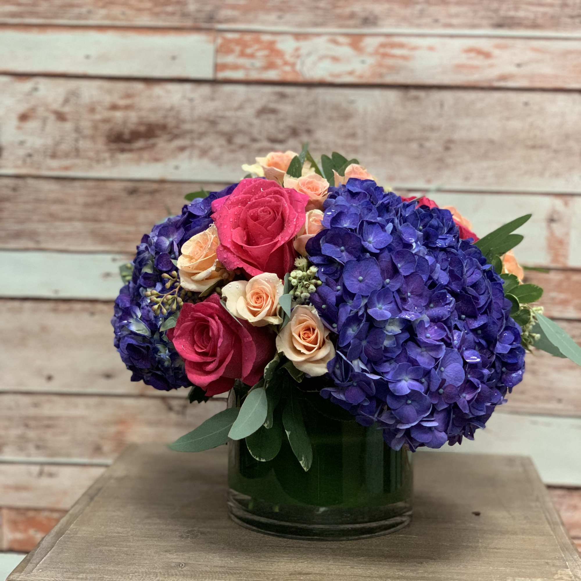 Deep purple hydrangeas and light colored roses make up this striking arrangement.
