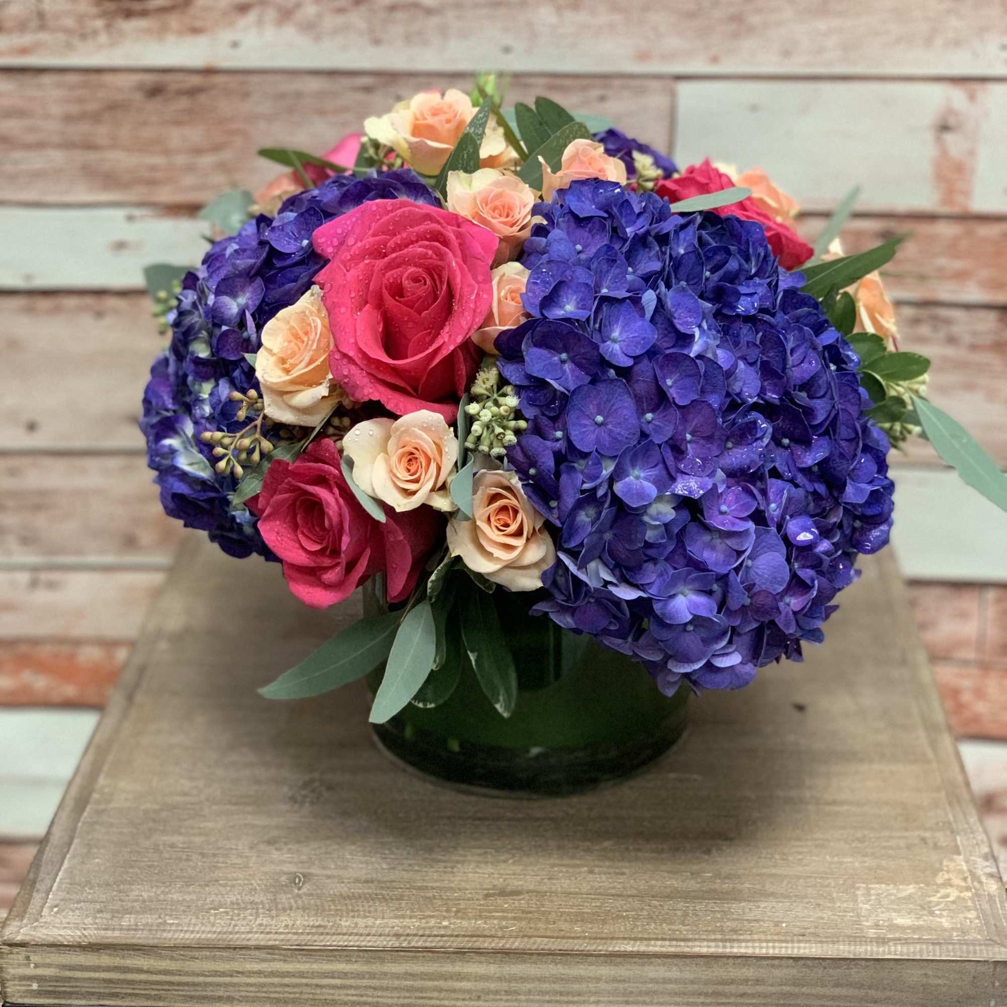 Deep purple hydrangeas and light colored roses make up this striking arrangement.